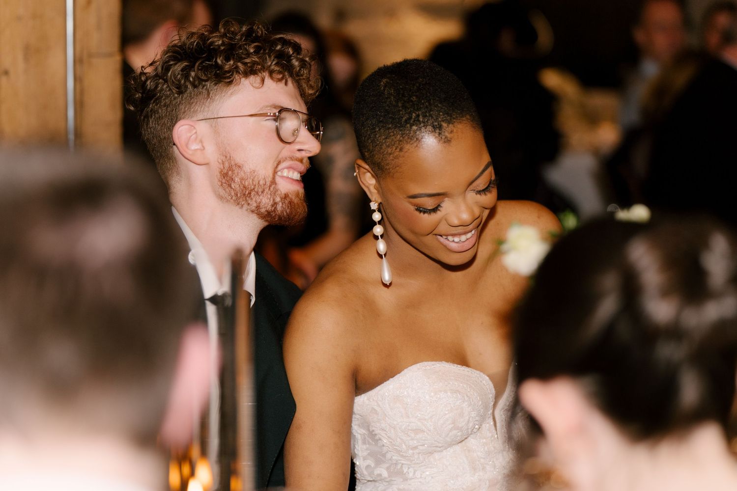 Bride in strapless gown laughs with groom in glasses at elegant Tapestry Hall wedding reception.
