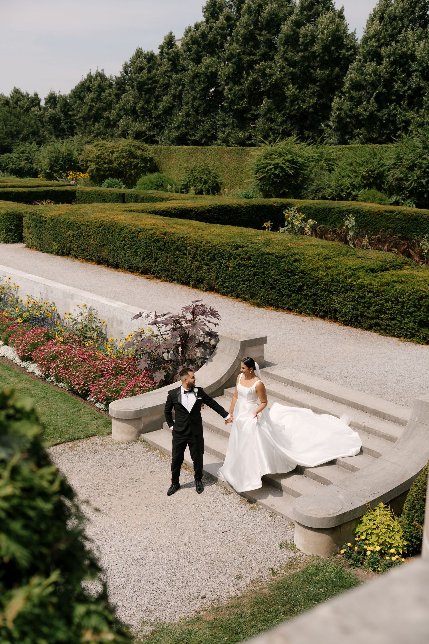 Aerial view of bride and groom holding hands on stone steps in elegant formal garden landscape at Parkwood Estates.