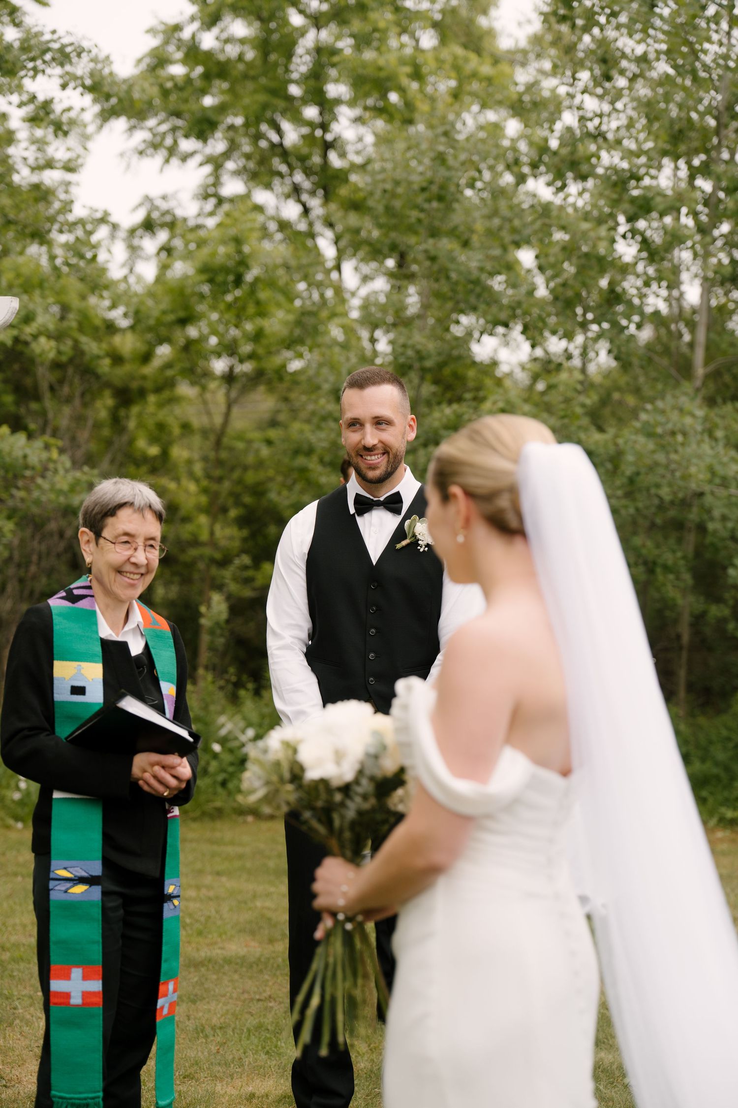 Bride approaches smiling groom and officiant during an intimate outdoor garden wedding ceremony at Guelph golf course.