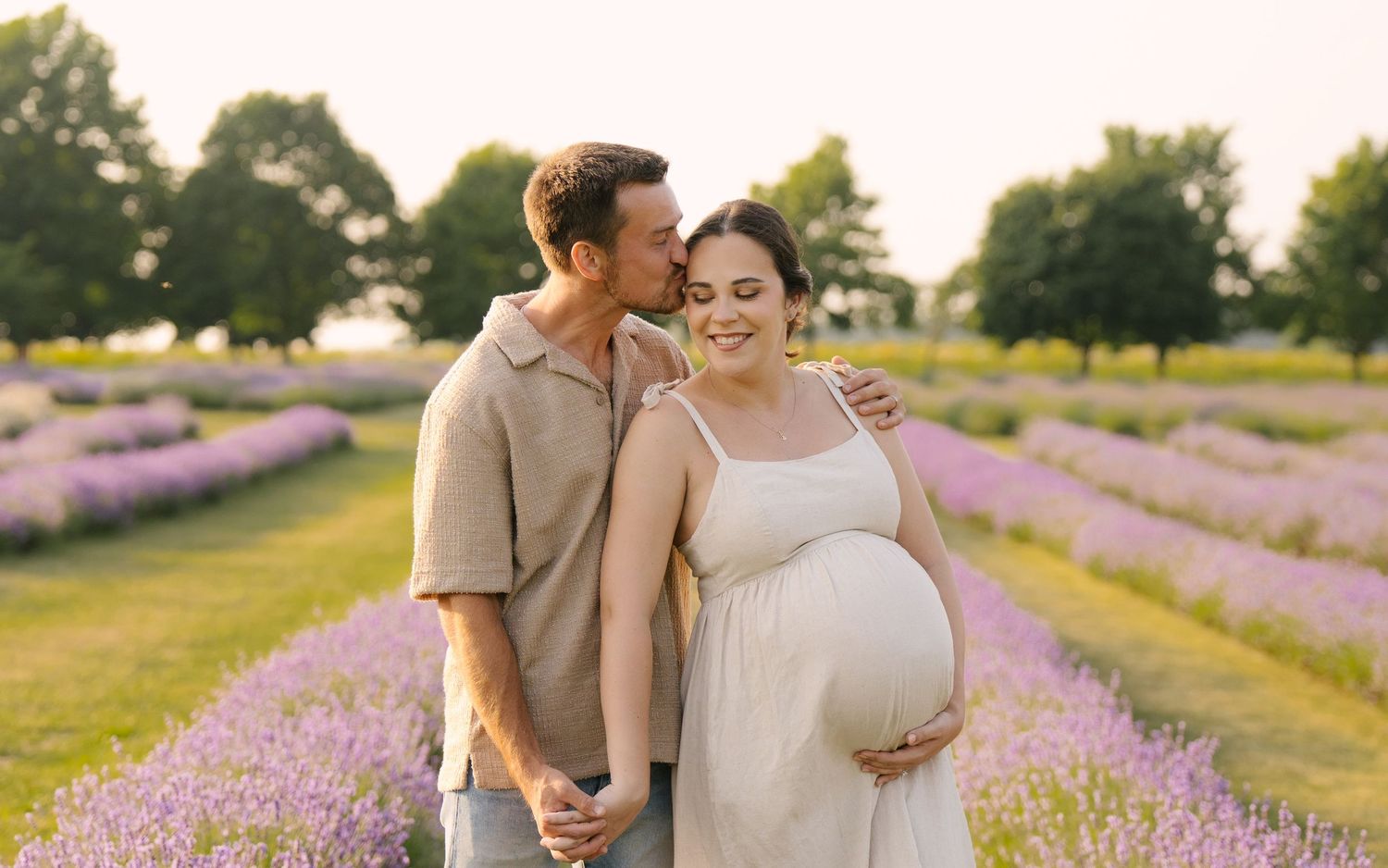 Happy pregnant woman and partner smiling together in blooming lavender field during golden hour sunset.