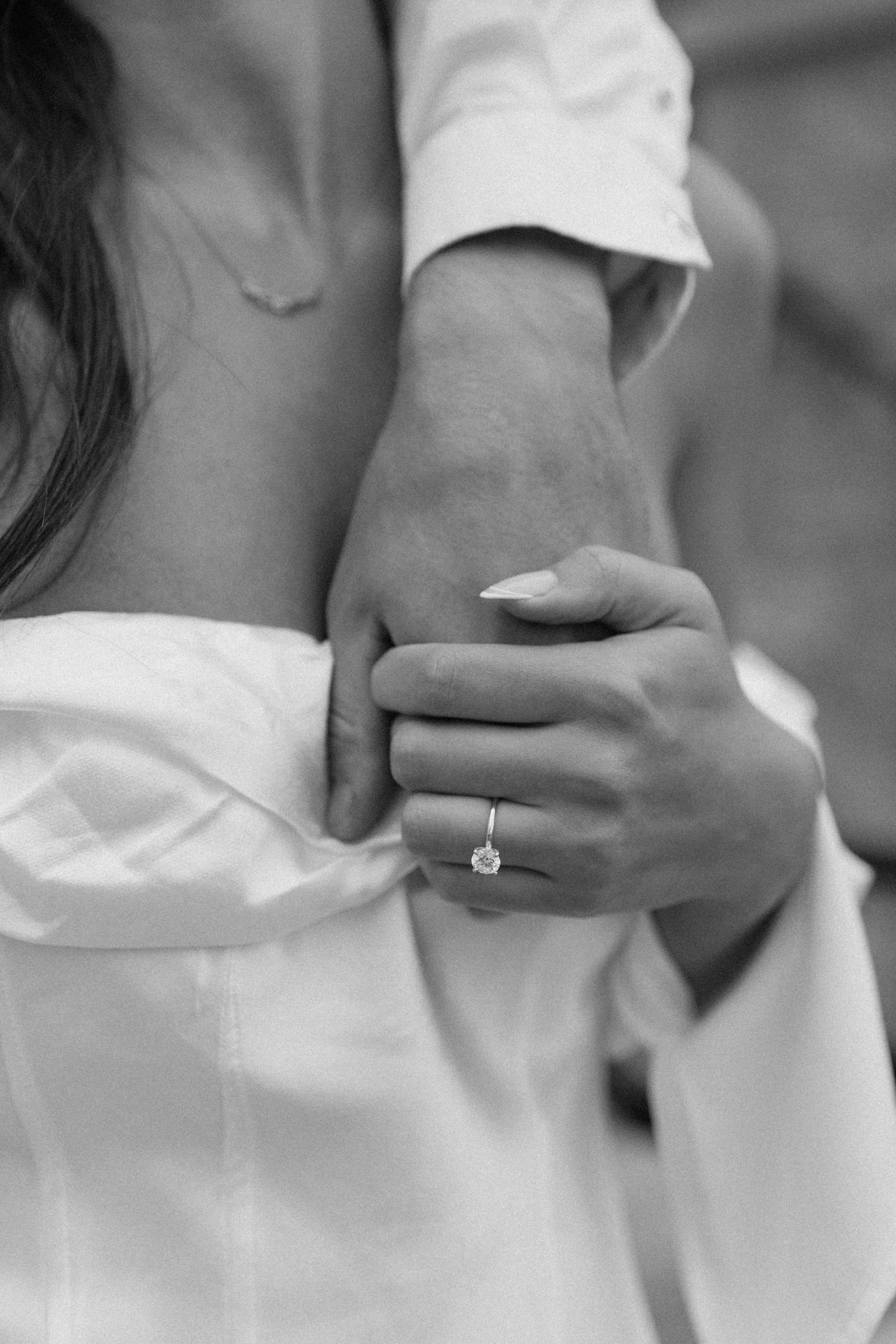 Black and white close-up of couple embracing, woman displaying diamond engagement ring.
