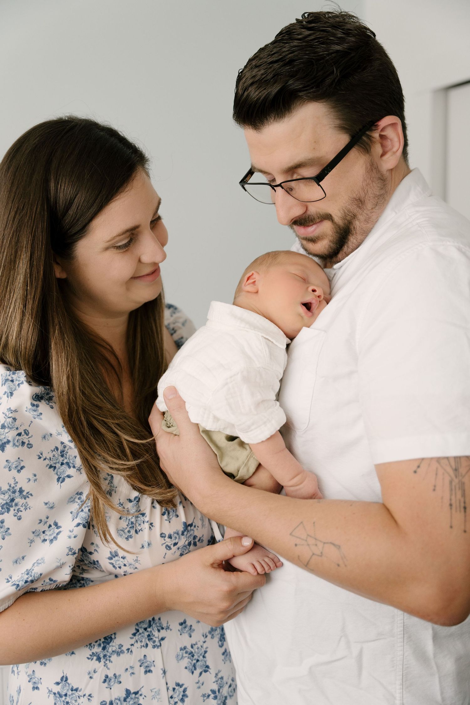 New parents lovingly gaze at their sleeping newborn baby together indoors.