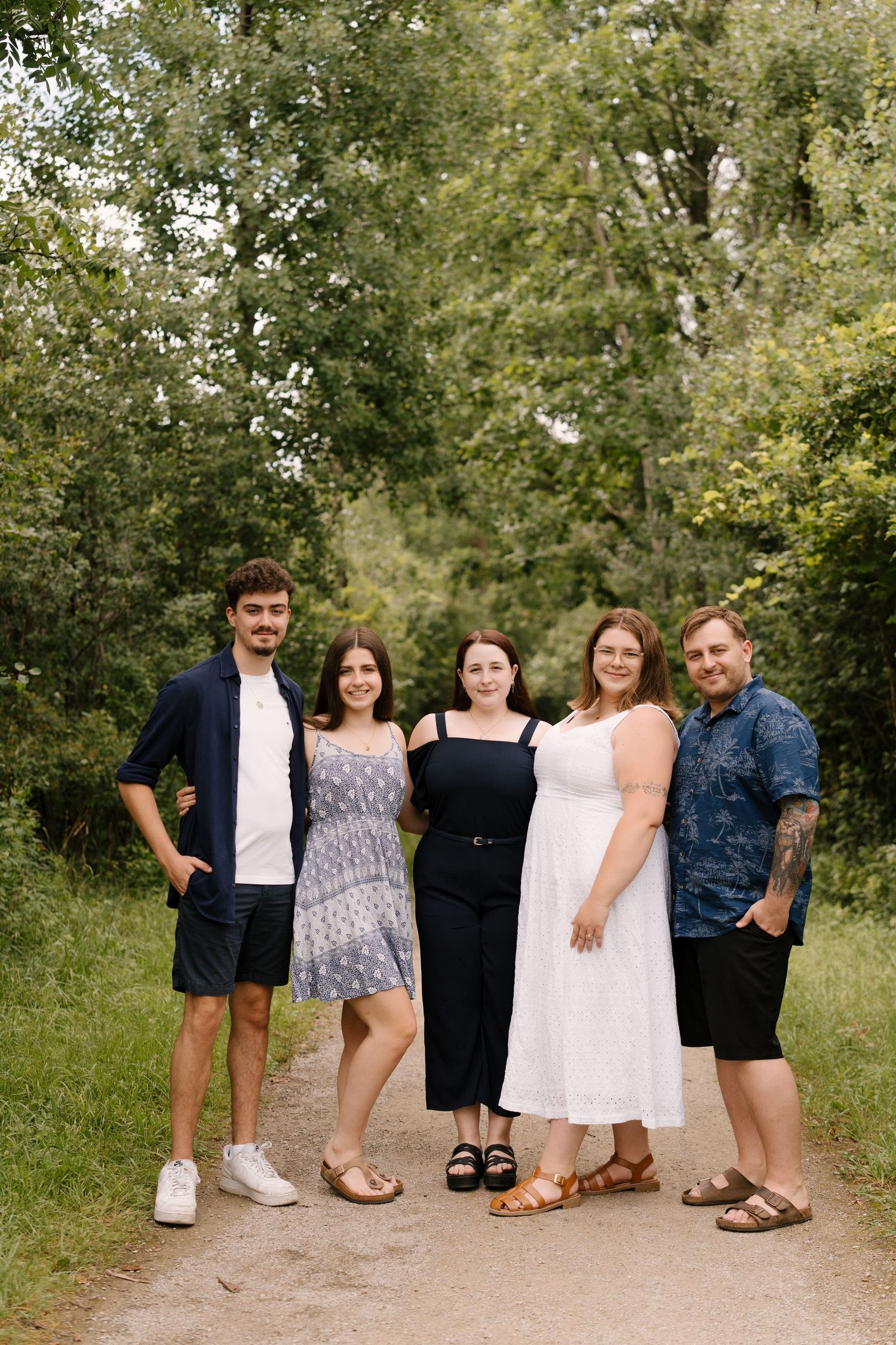 Five young adults posing together on a nature trail surrounded by green trees.