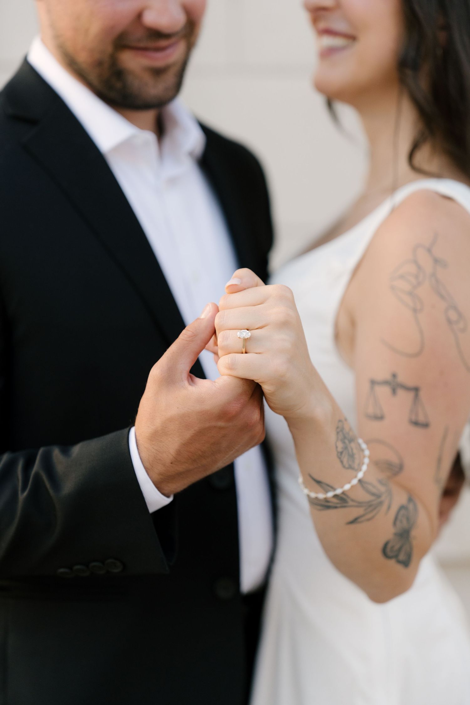 Close-up of couple holding hands showing bride's diamond engagement ring and arm tattoos.
