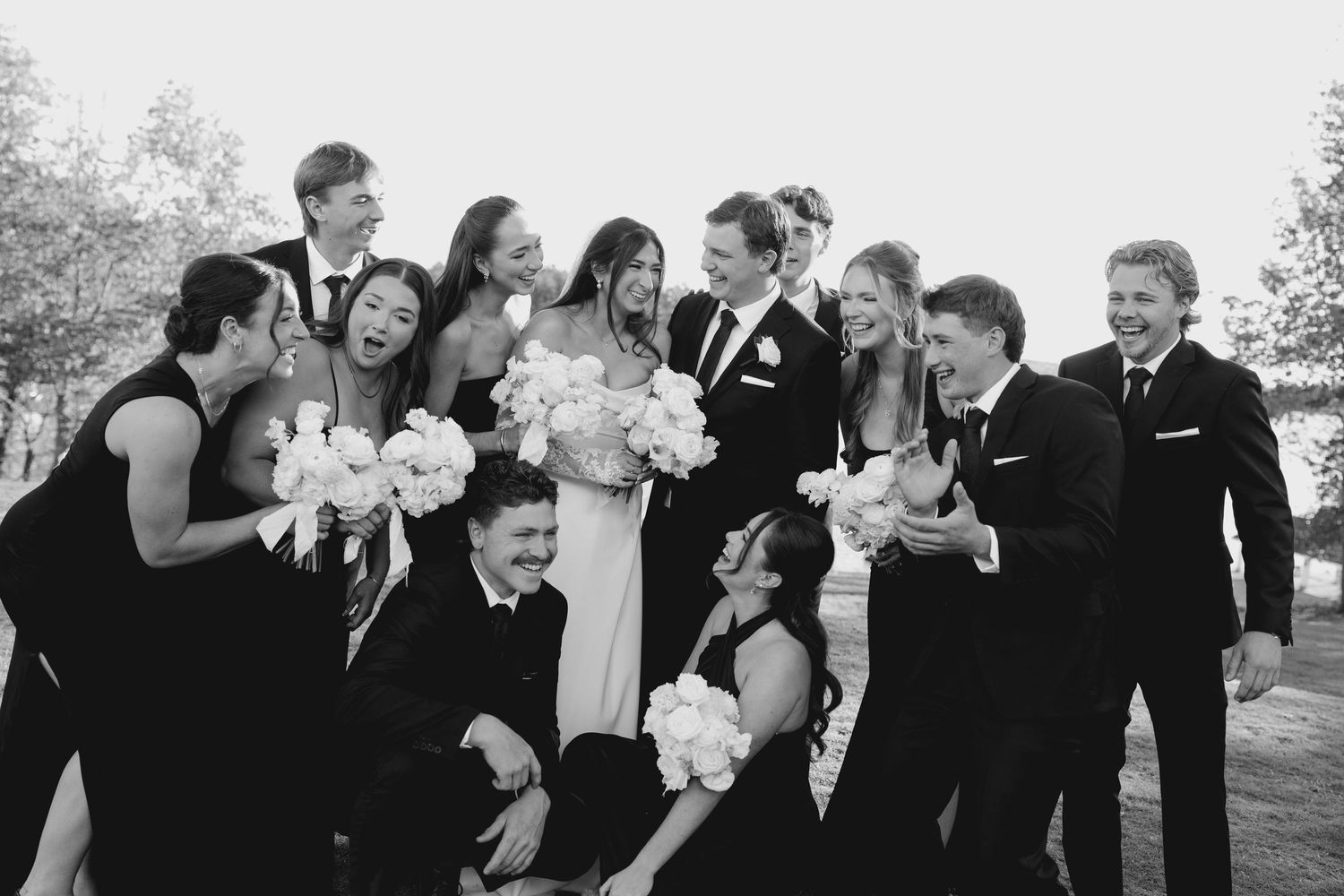 Black and white photo of laughing wedding party group gathered together outdoors on wedding day.