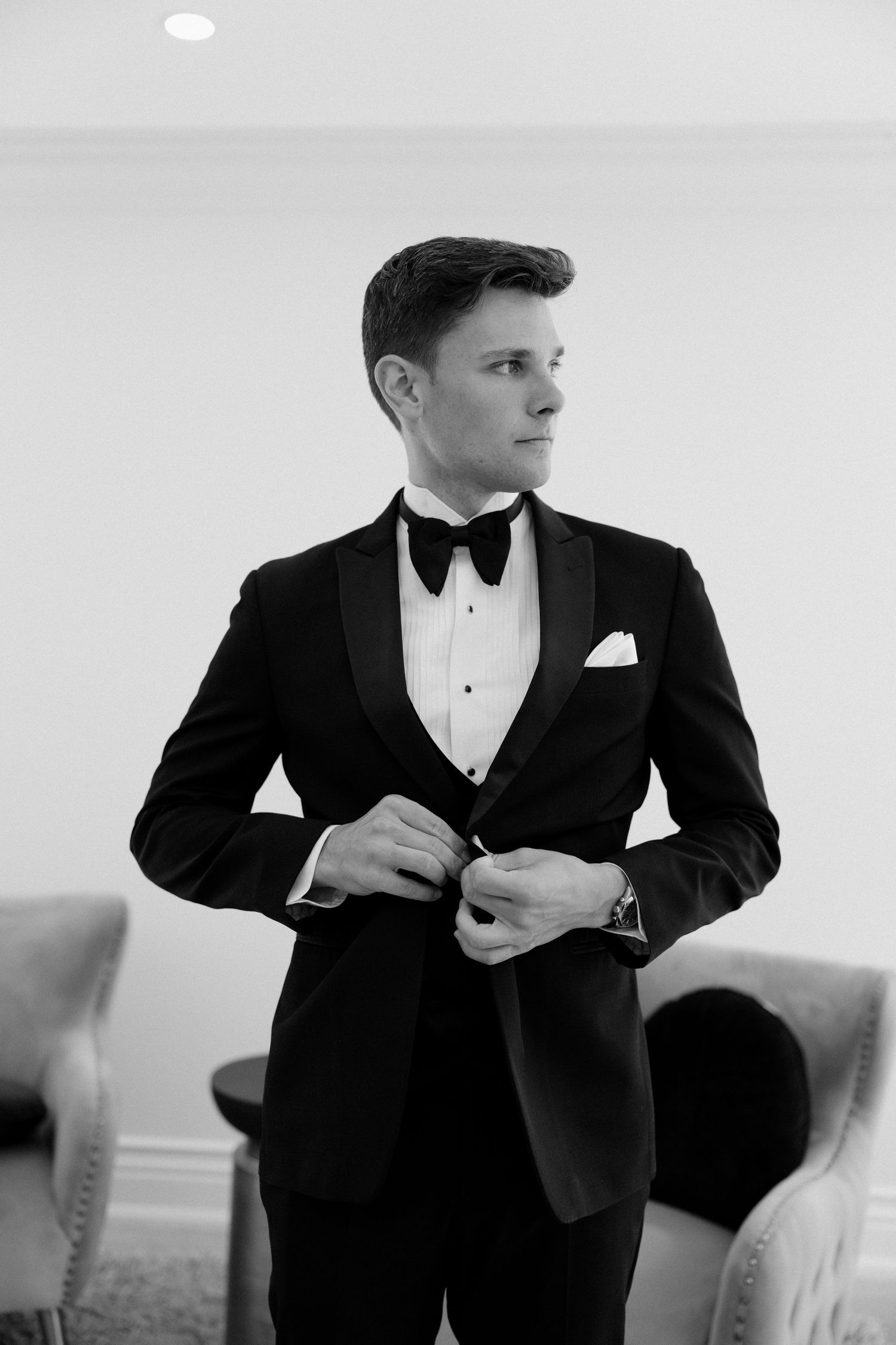 Groom in black tuxedo with bow tie buttoning jacket in elegant black and white wedding preparation photo at Roseville Estates wedding venue.