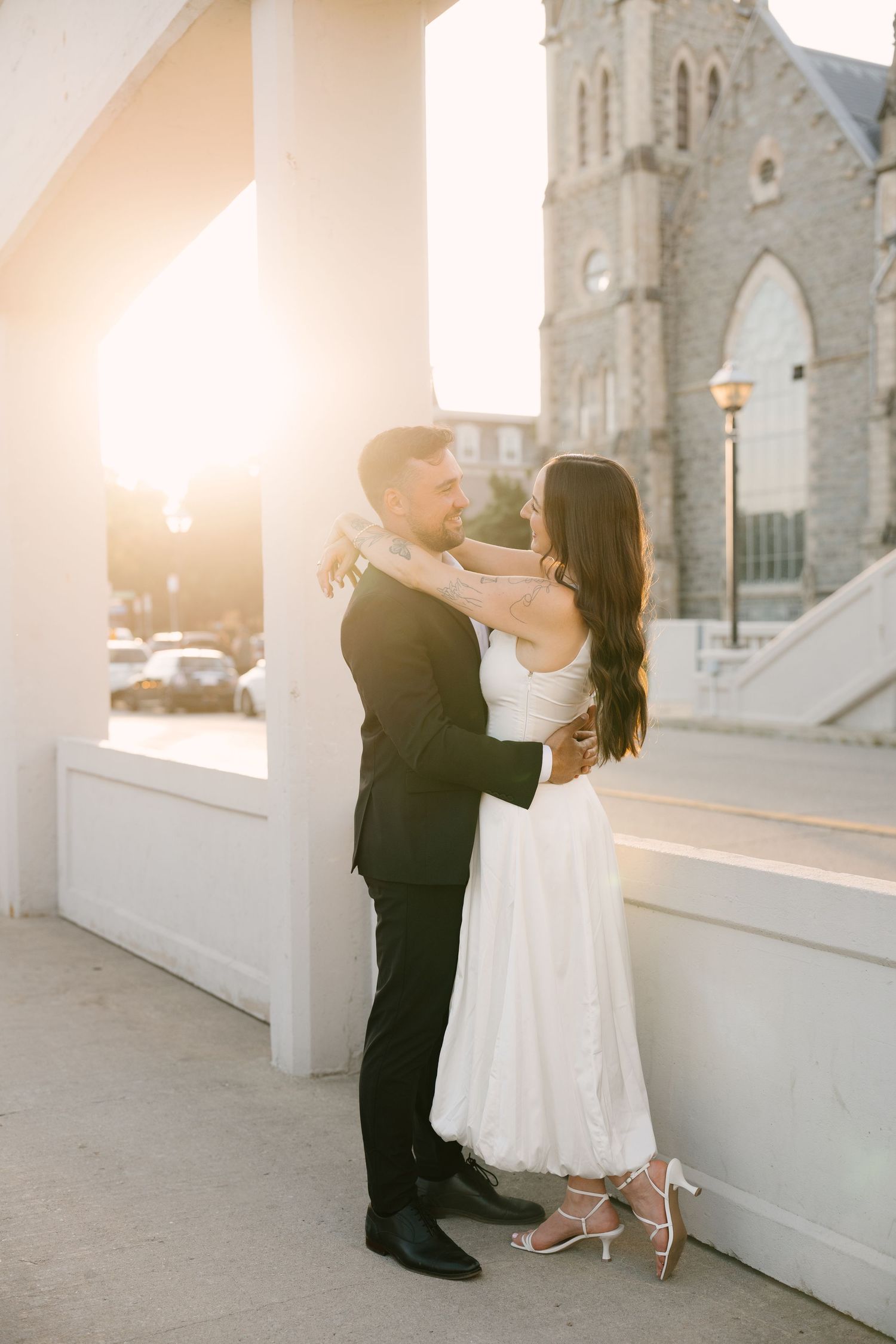 Newlyweds embracing in warm golden sunset light with a stone church in the background.
