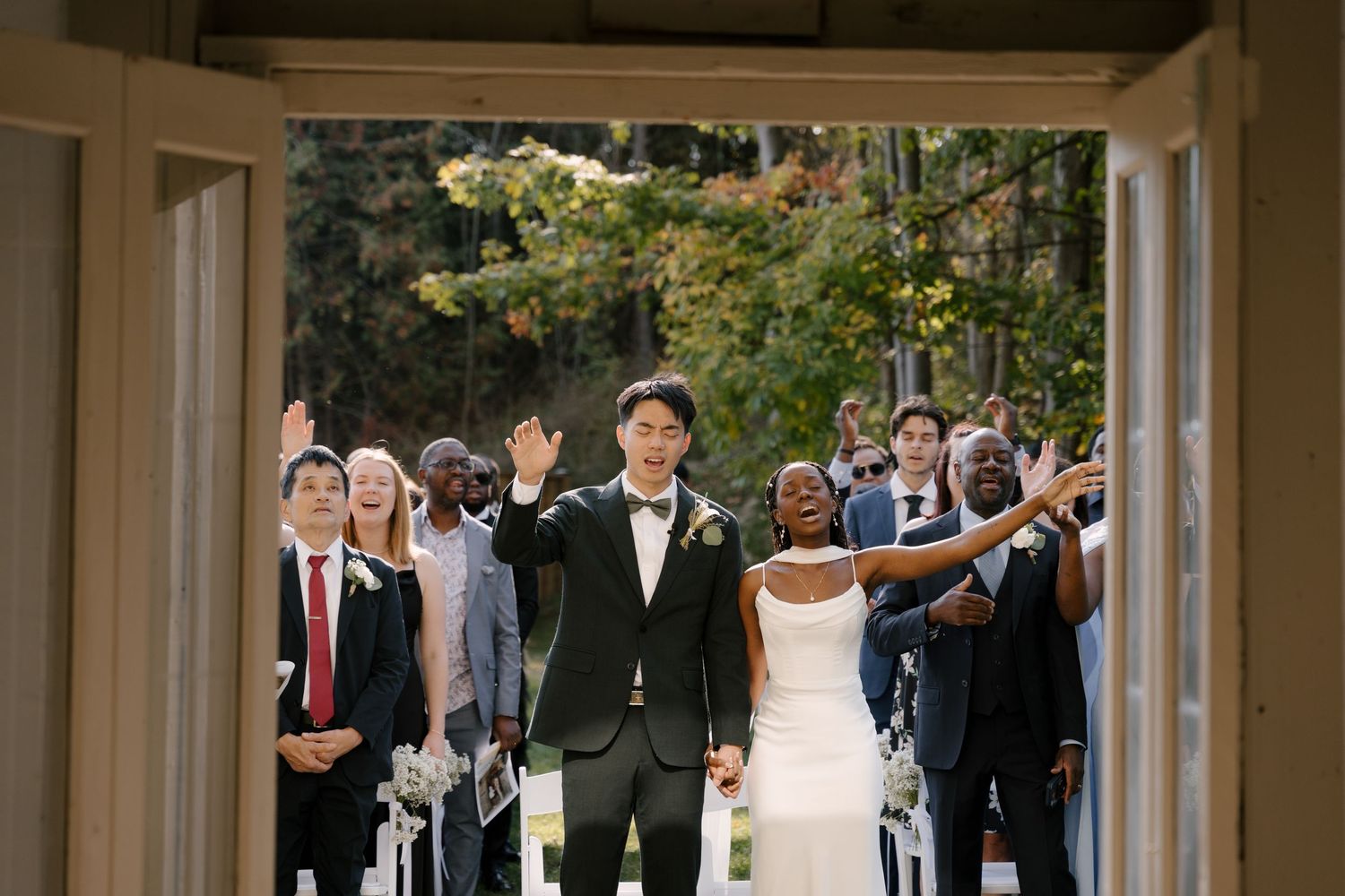 Interracial newlyweds walk joyfully through venue doors as guests celebrate behind them at Wren House.