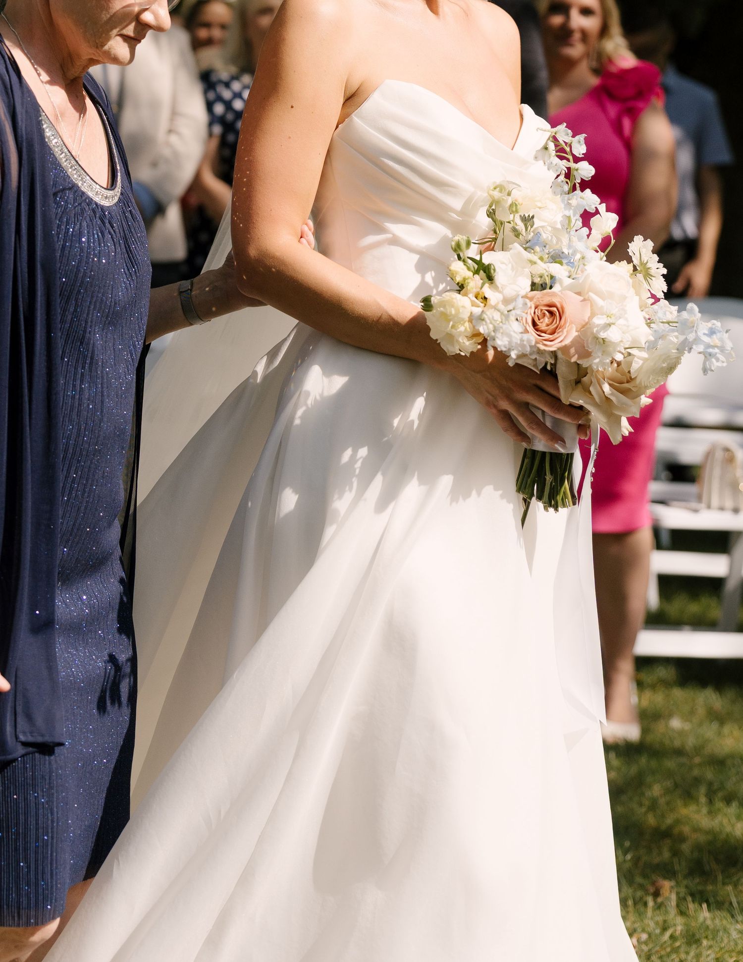 Bride holding a lush white and blush bouquet of roses and hydrangeas while walking down the aisle.