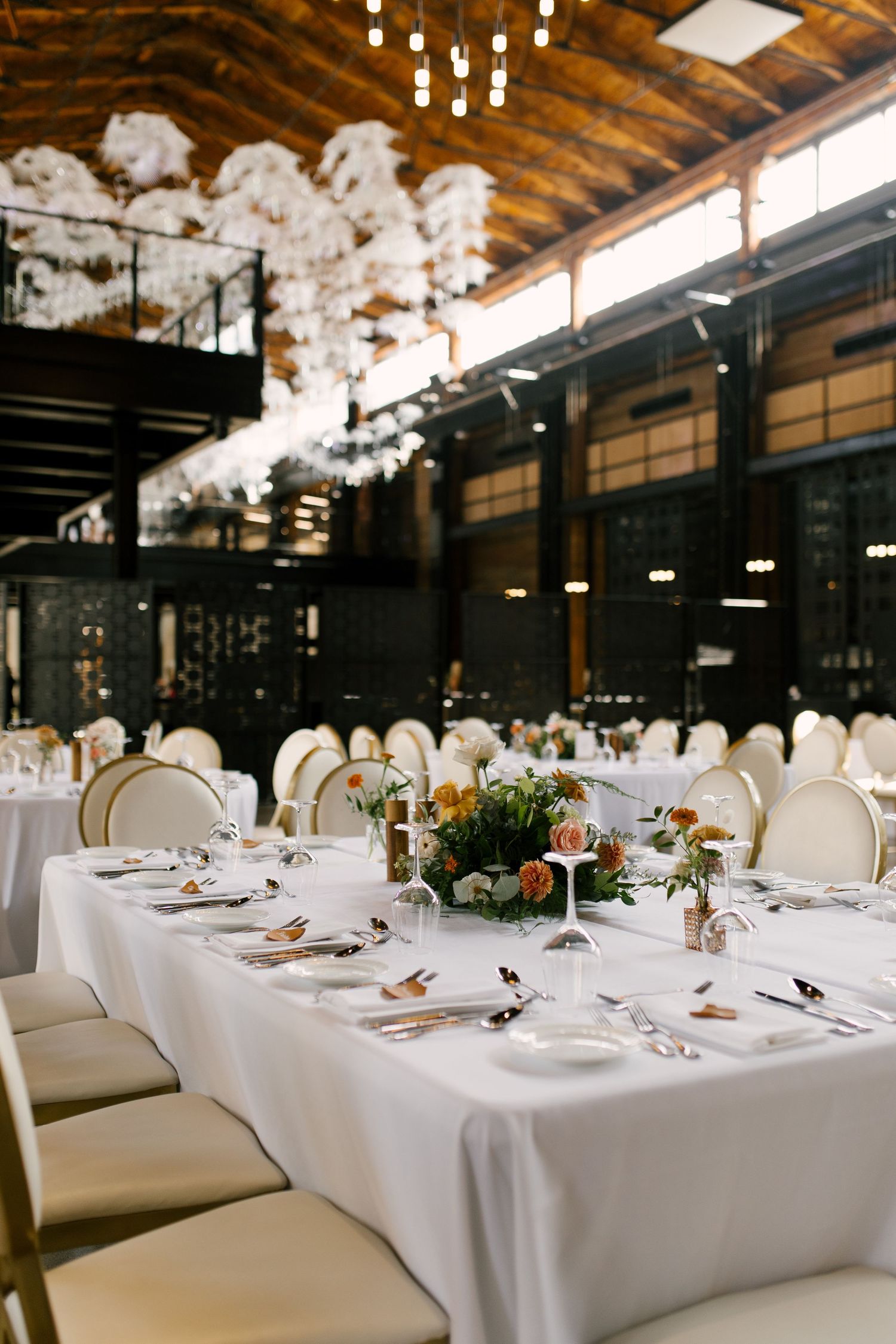 Sophisticated Tapestry Hall wedding reception hall with white draped tables, gold chairs, and floral centrepieces under warm lighting.
