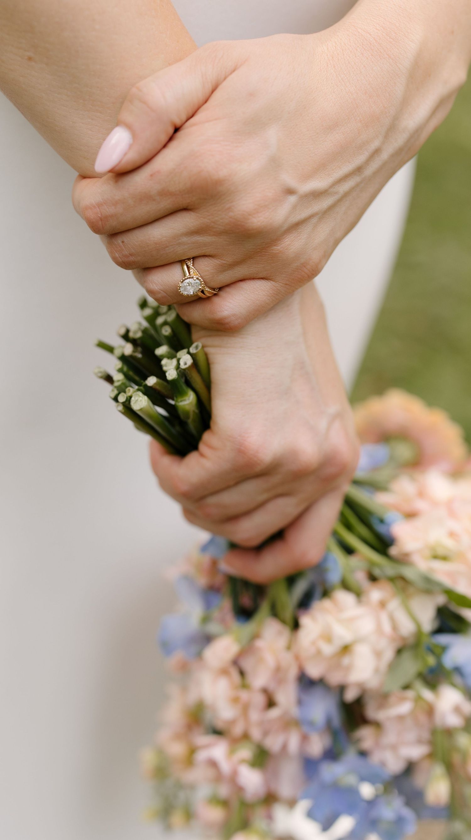 Close-up of bride's gold diamond engagement ring while holding a delicate bouquet of pastel flowers.