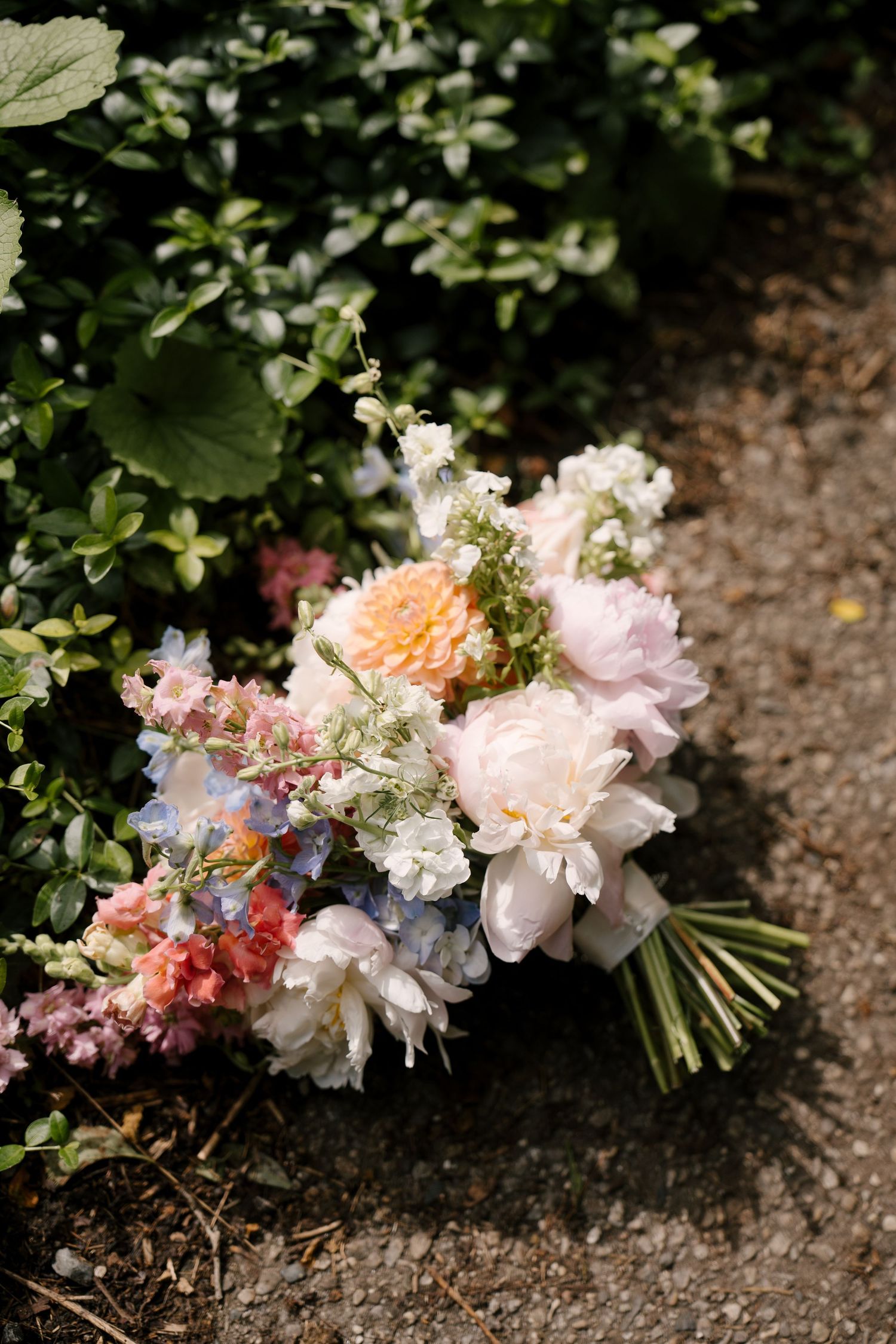 Romantic bridal bouquet with pink peonies, coral dahlias, and wildflowers resting on garden path.
