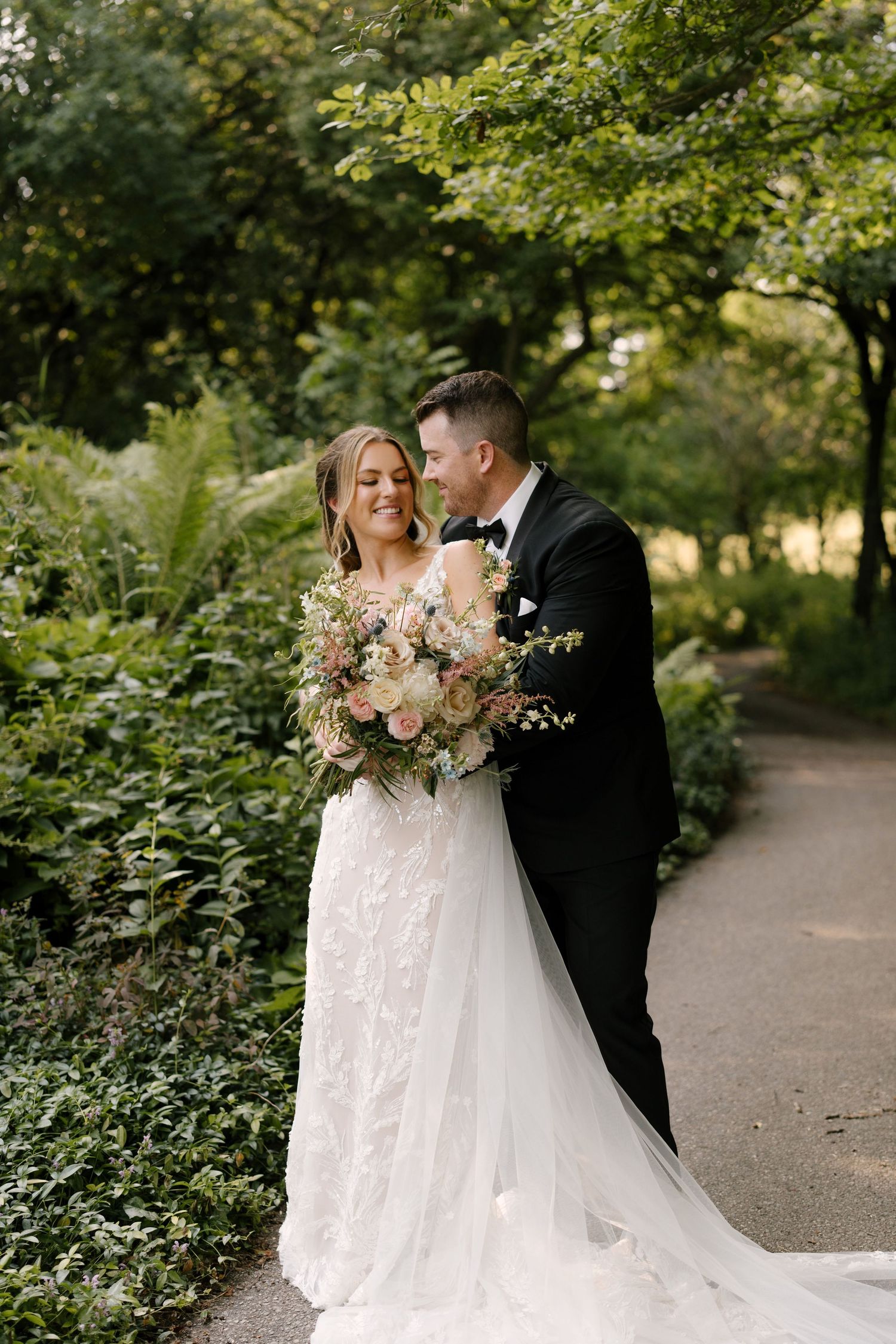 Smiling bride and groom standing together on a garden path surrounded by lush green foliage at St Marys wedding venue.