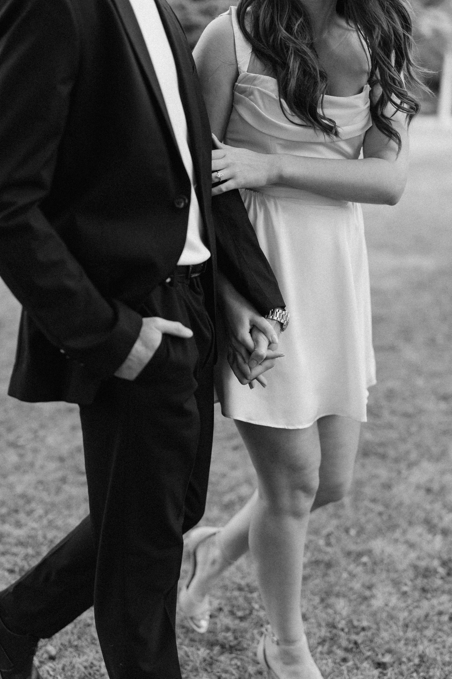Black and white close-up of couple walking together holding hands outdoors.