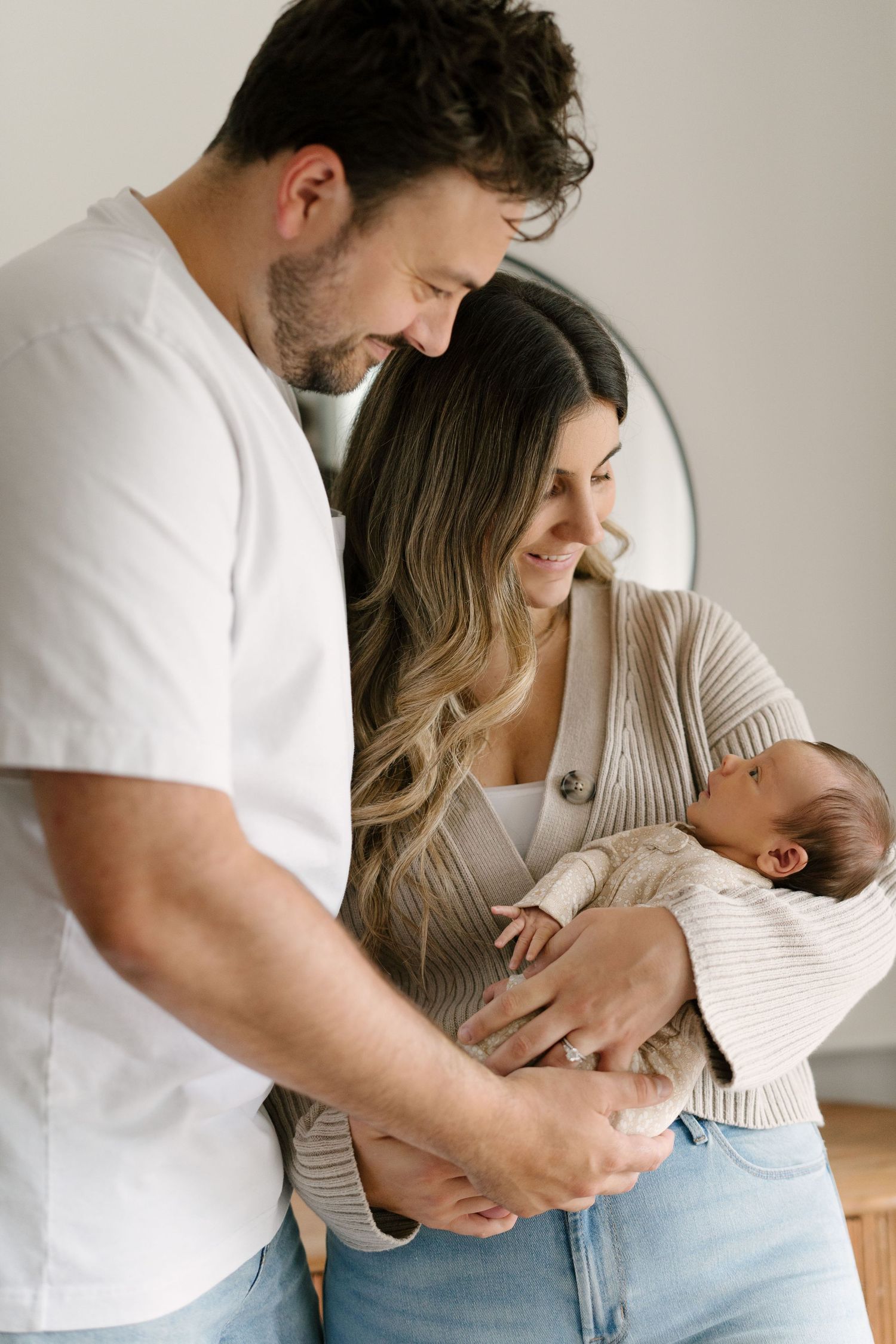 A couple smiles lovingly at their newborn baby, with the mother cradling the infant in a warm, bright room.