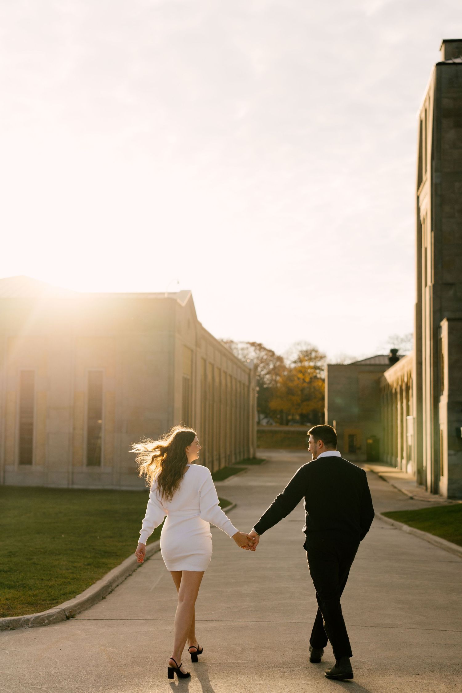 Couple holding hands strolling along a path bathed in warm golden sunset light.