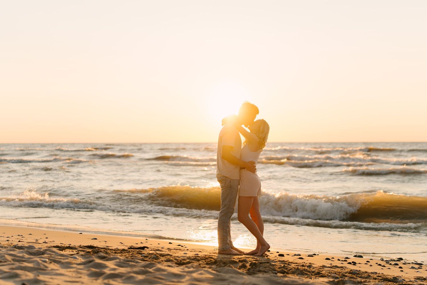 Silhouetted couple kissing on sandy beach at vibrant golden sunset with ocean waves behind.