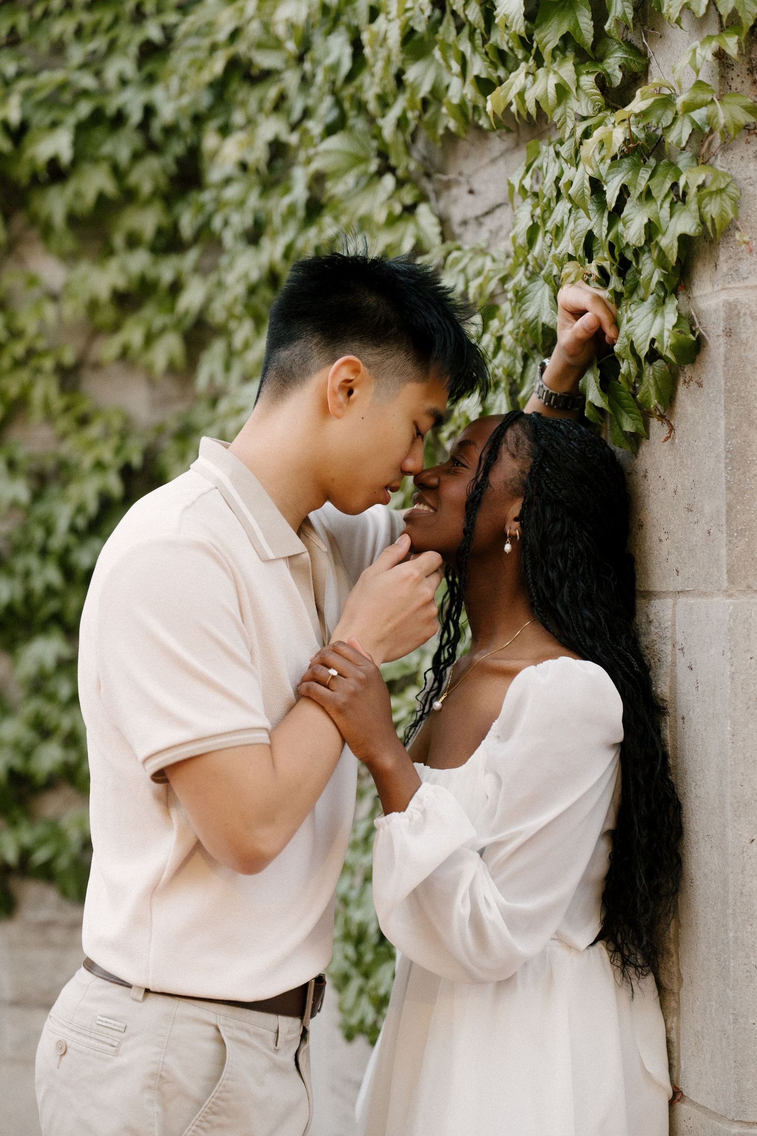 Couple sharing an intimate moment against an ivy-covered stone wall, holding hands and touching foreheads.