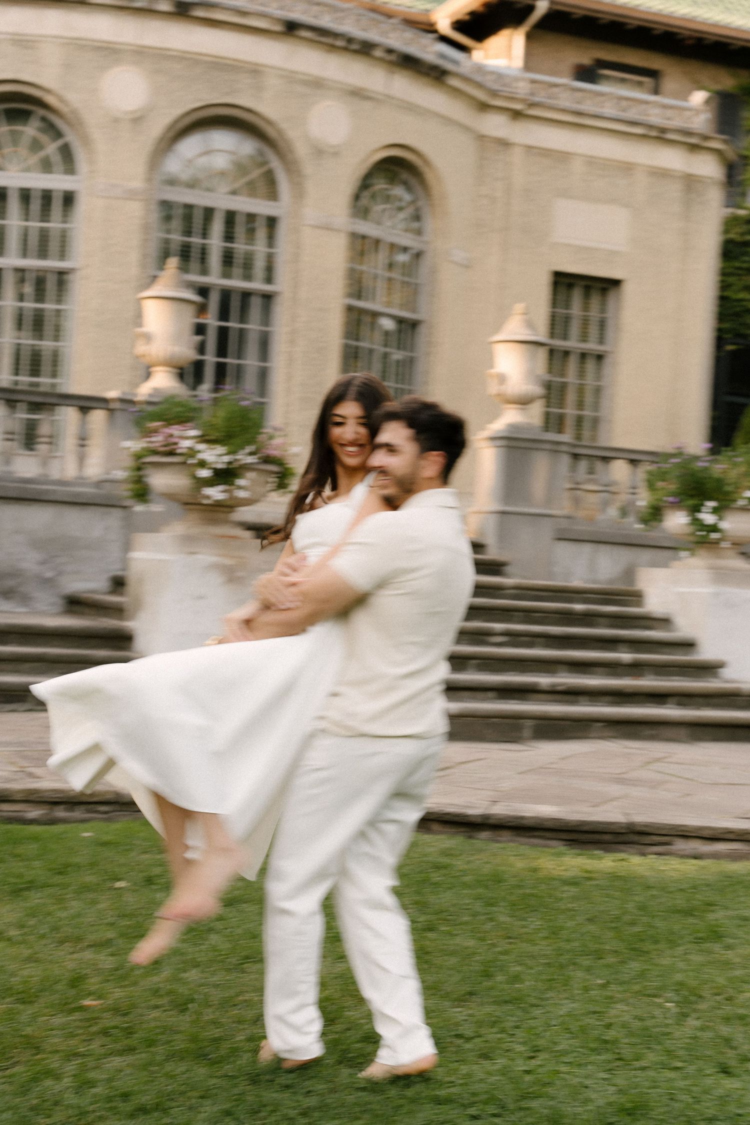 Couple spinning joyfully outdoors with motion blur effect in front of a grand historic building.