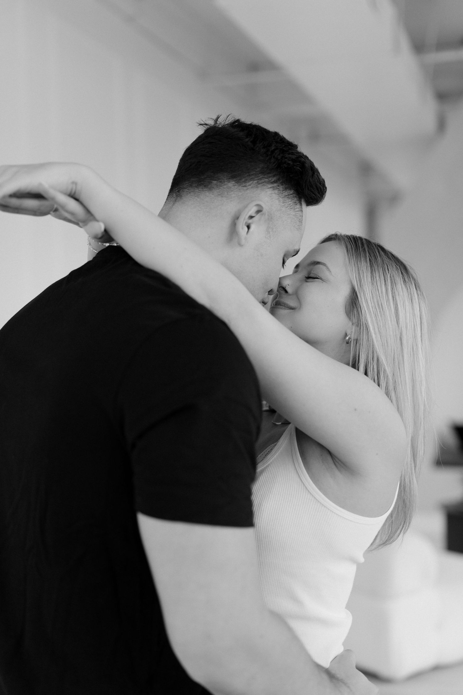 Black and white romantic photo of couple sharing a kiss, woman embracing man in a tender moment.