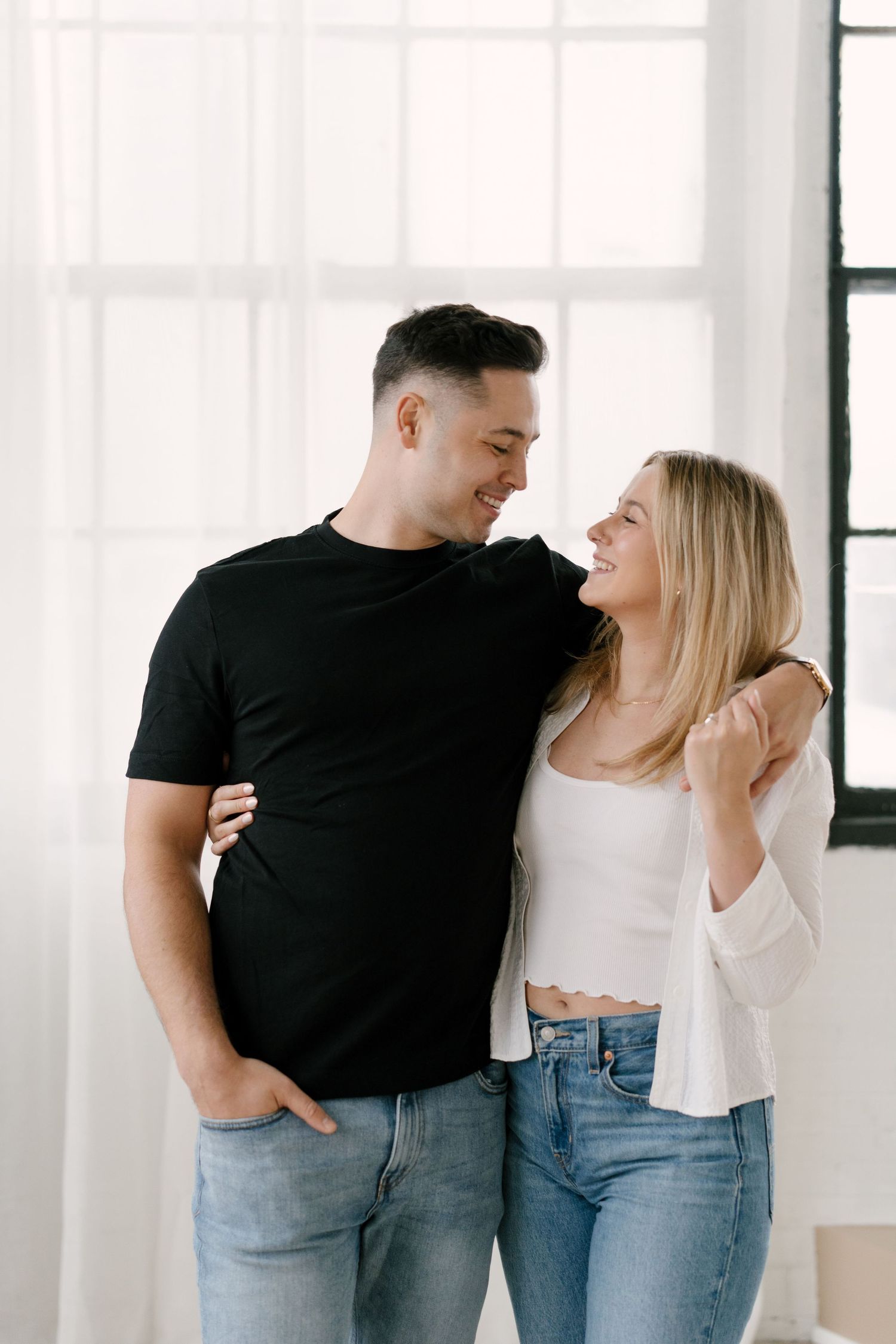 Smiling couple in casual jeans embracing and looking at each other in a bright white room.
