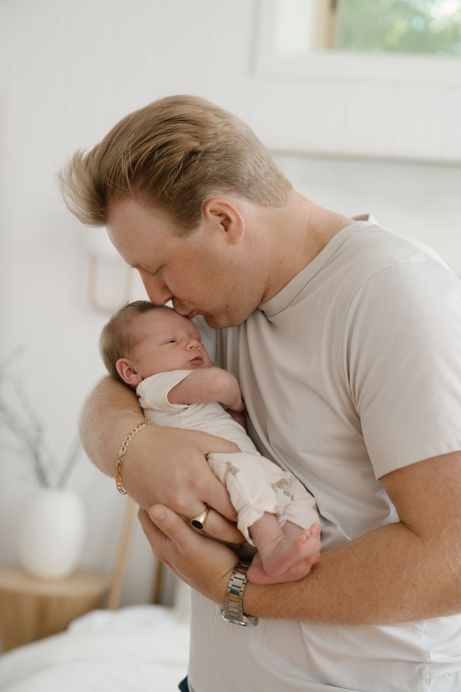 Loving father kissing newborn baby gently on forehead in white room.