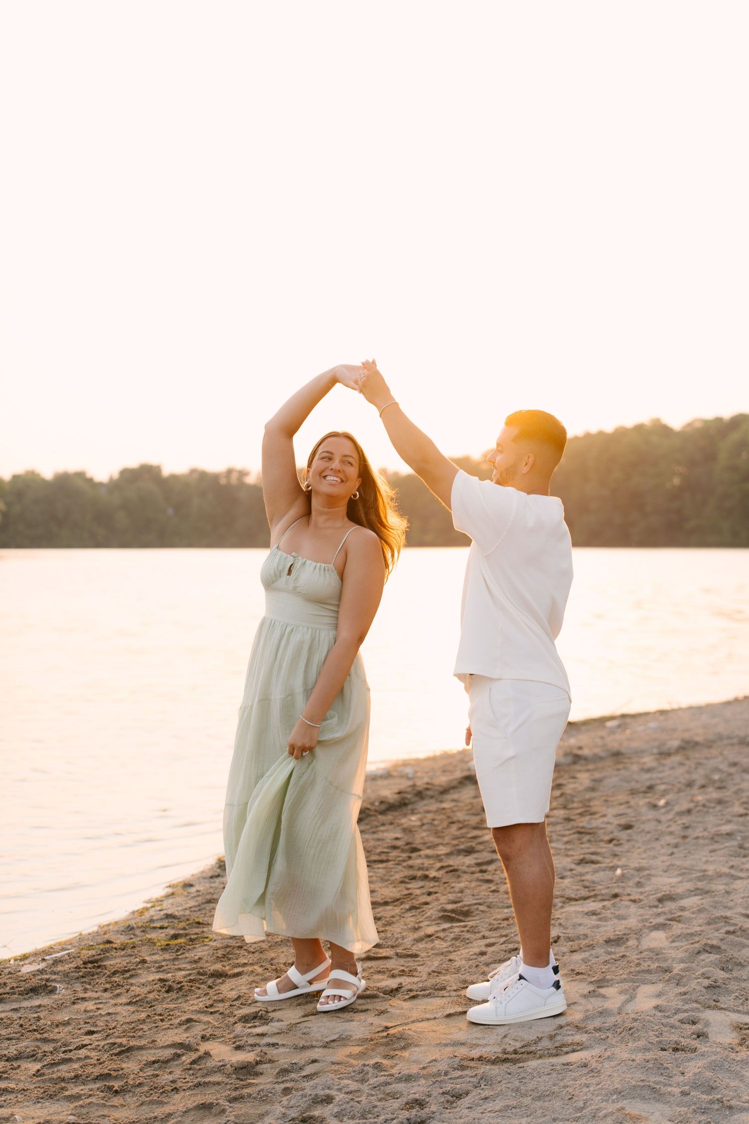 Joyful couple dancing on beach shore during warm golden sunset by the lake.