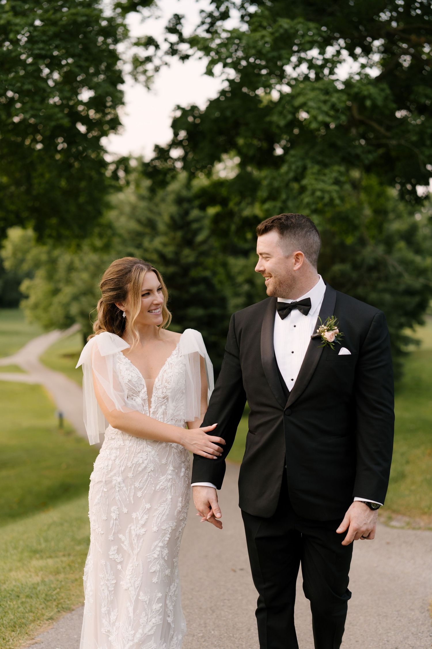 Happy bride and groom walking hand in hand along a scenic tree-lined path on their wedding day.