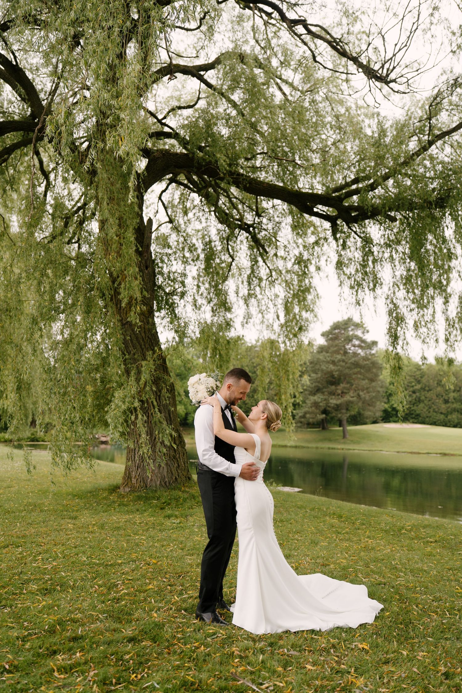 Newlyweds share a romantic moment under a sweeping weeping willow tree beside a serene pond in Guelph.