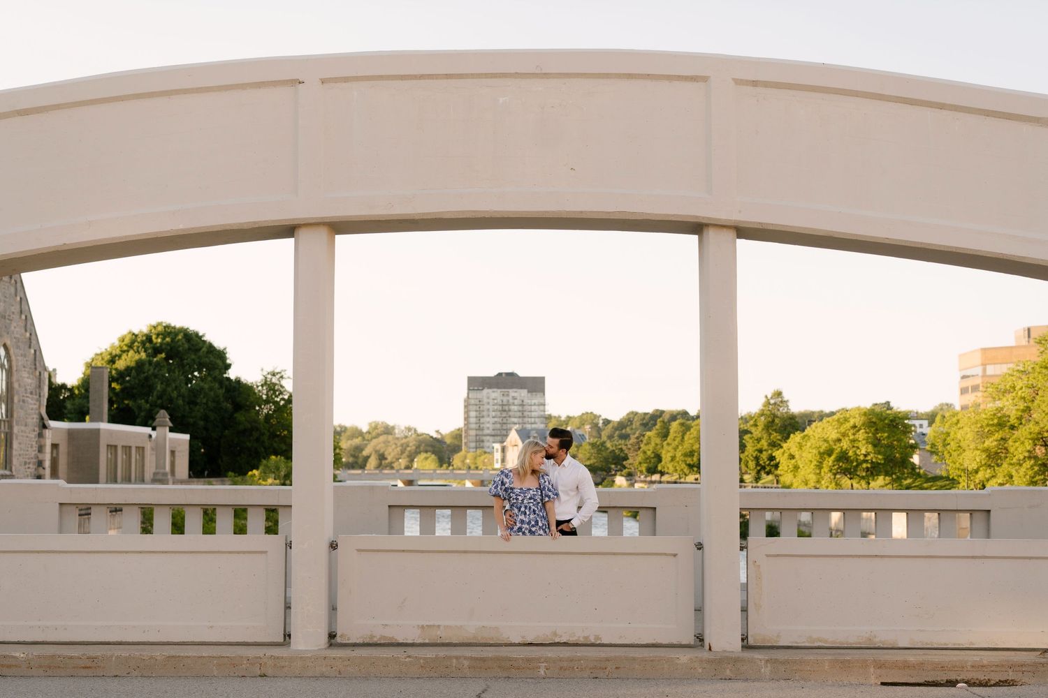 Couple embracing under white arched bridge structure outdoors.