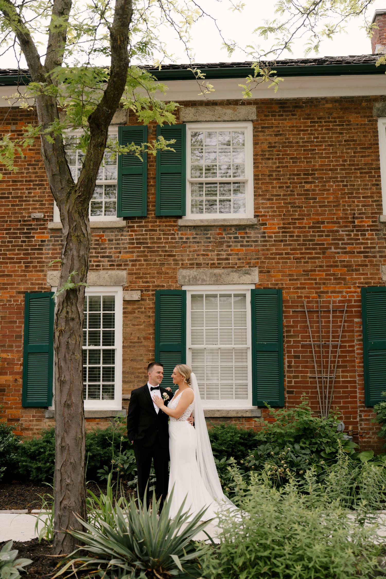 Bride and groom share a romantic moment outside a historic red brick building with green shutters at Niagara on the lake.