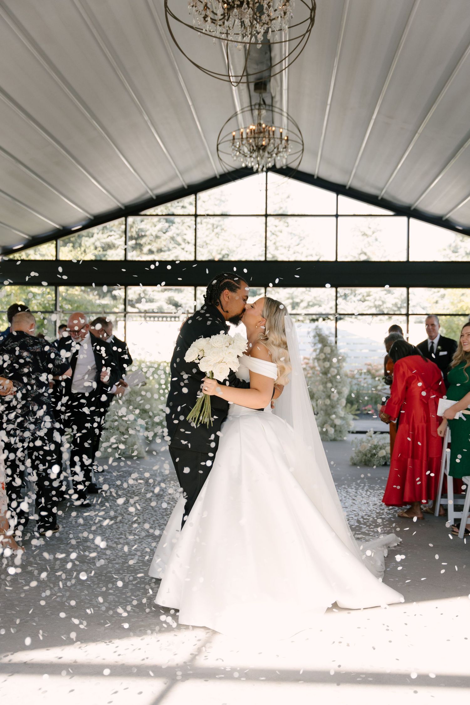 Bride and groom share first kiss as confetti falls during indoor wedding ceremony at Whistle Bear wedding venue.