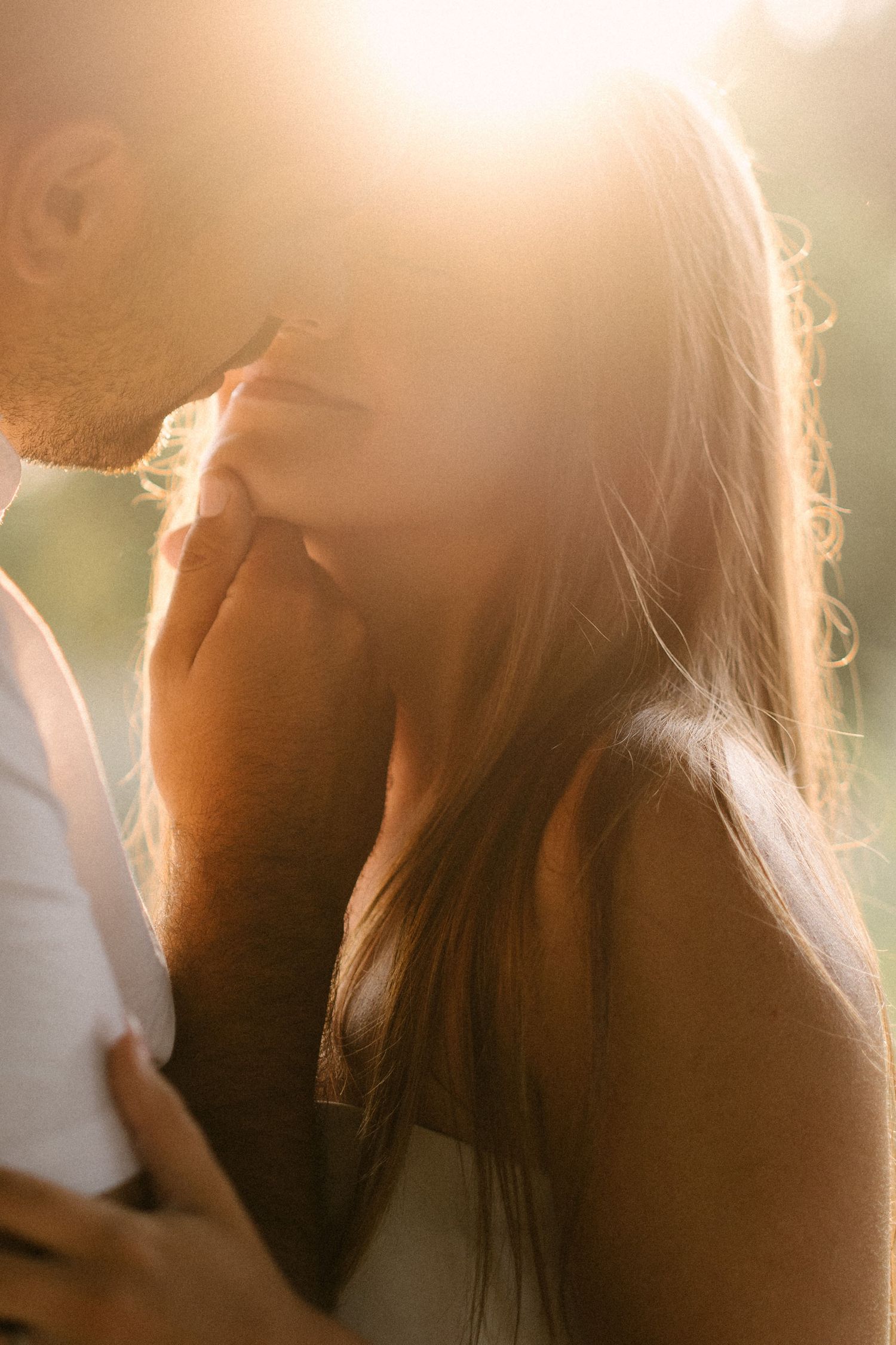 Close-up of couple sharing an intimate moment bathed in warm golden sunlight with soft bokeh background.
