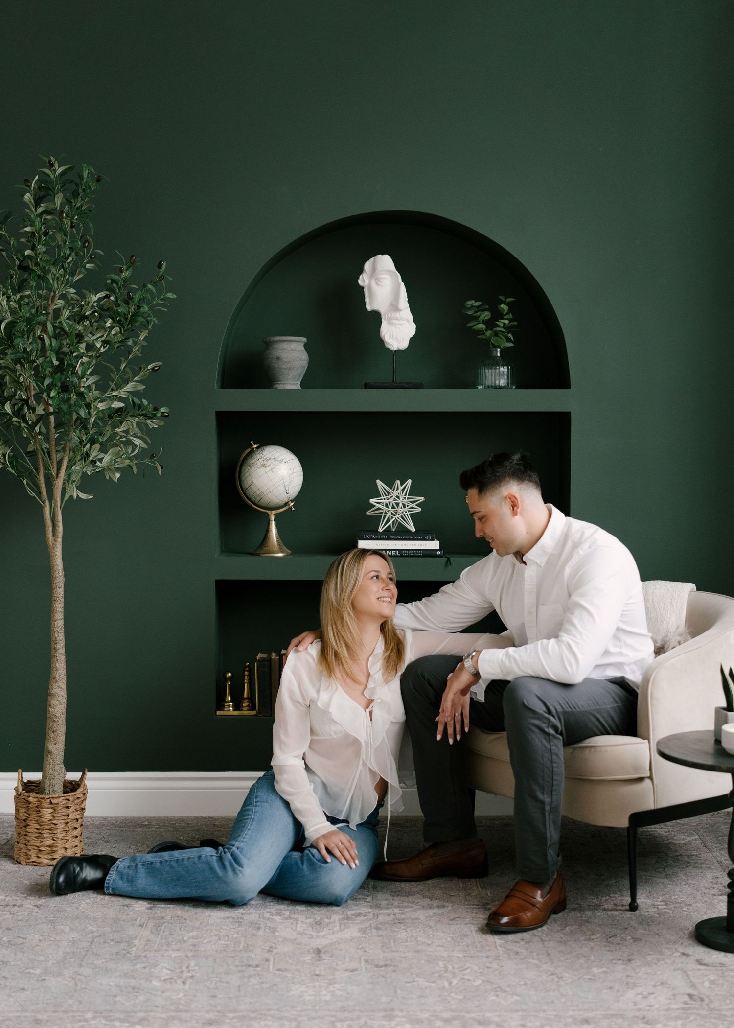 Couple sharing a relaxed moment on a couch and floor in an elegant dark green interior room.
