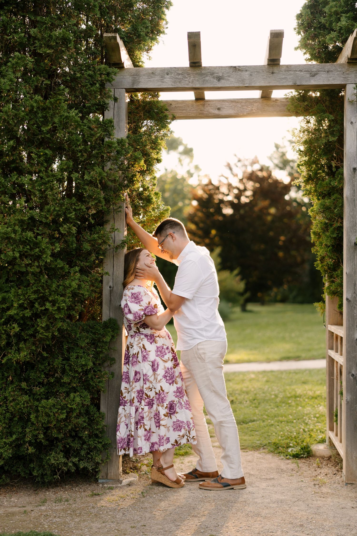 Couple sharing tender moment under rustic wooden garden arbor with ivy at golden sunset.