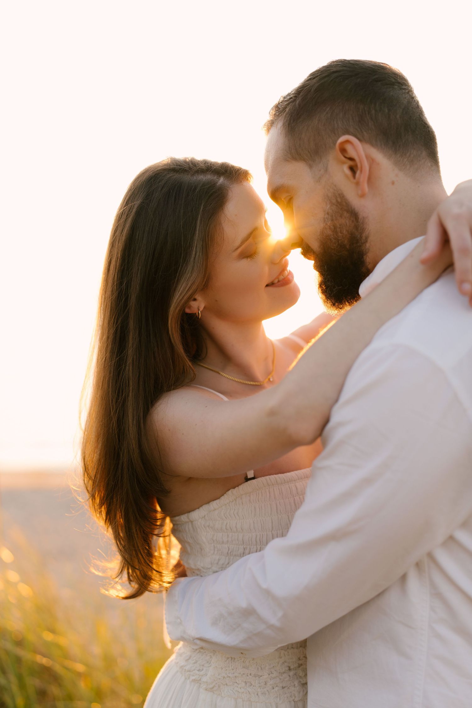 Close-up of romantic couple almost kissing in warm golden sunset light outdoors.