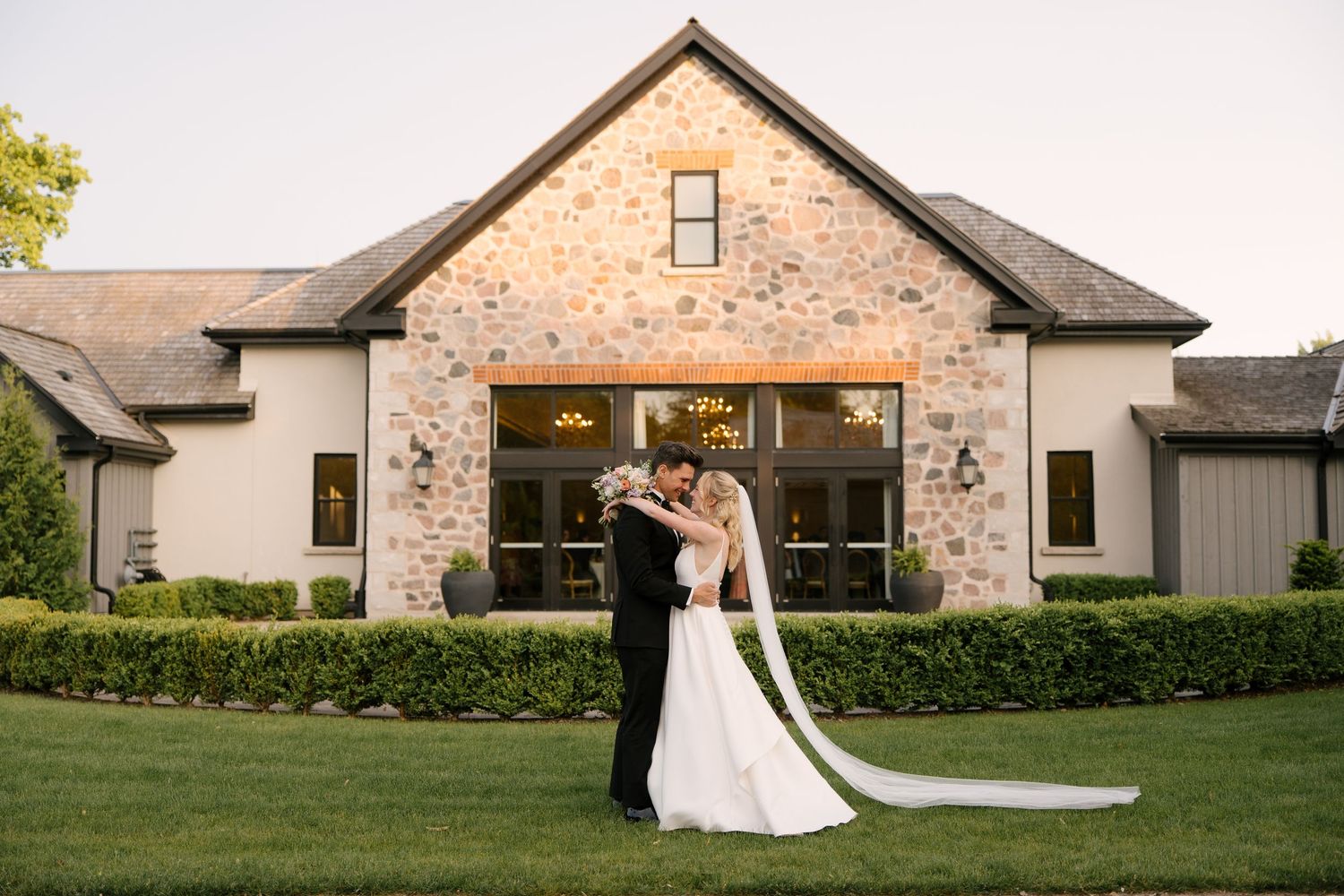 Bride and groom sharing a romantic embrace in front of an elegant stone at Roseville Estates wedding venue.