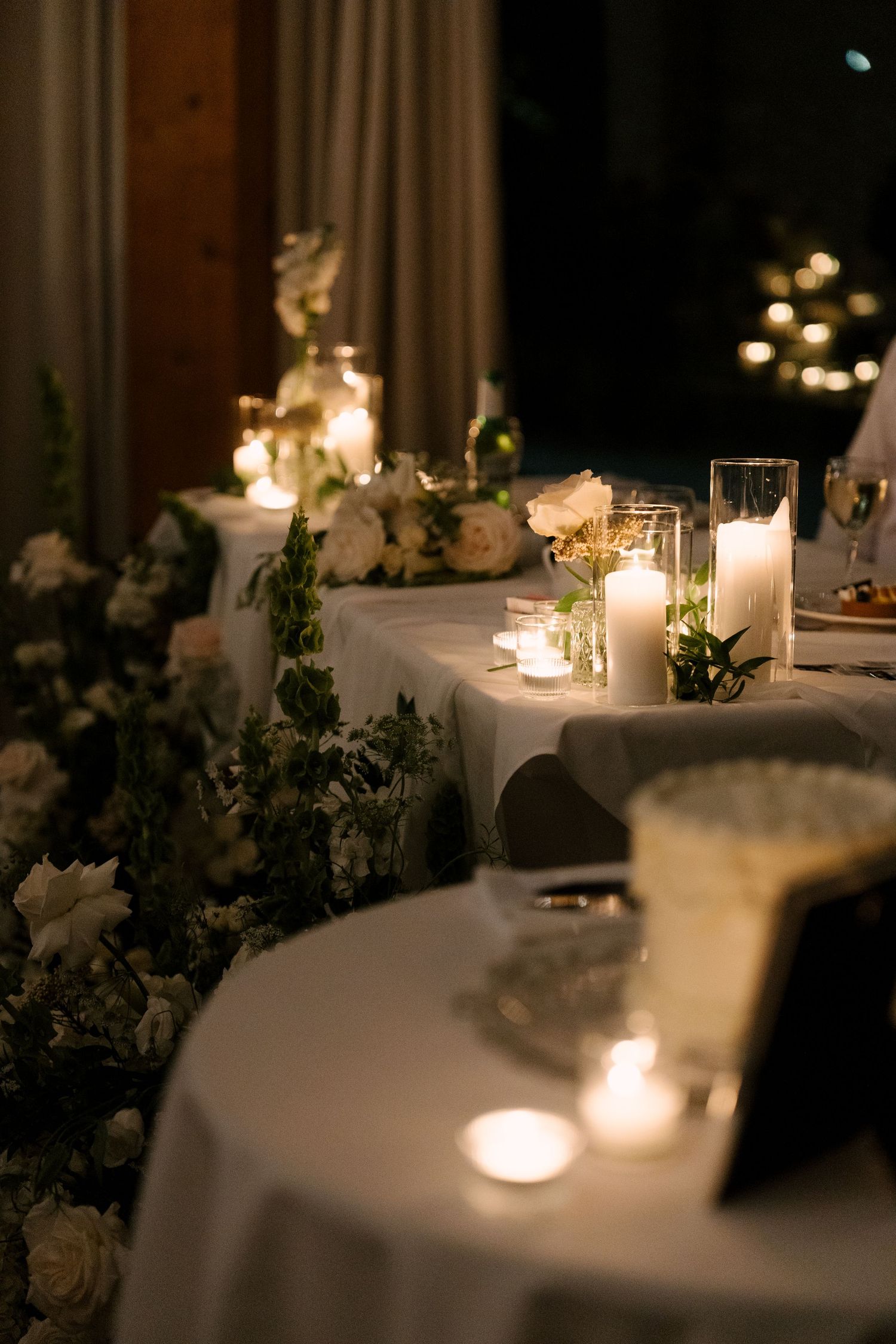 Elegant wedding reception table with white candles, roses, and greenery garland in soft candlelight at Pillar and Post.
