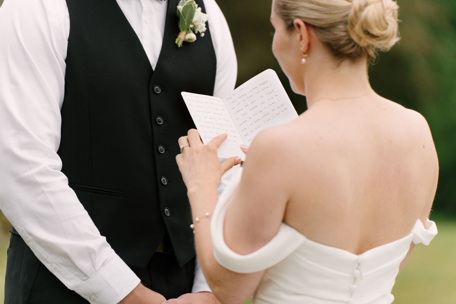 Bride reading handwritten vows to groom during intimate outdoor wedding ceremony.
