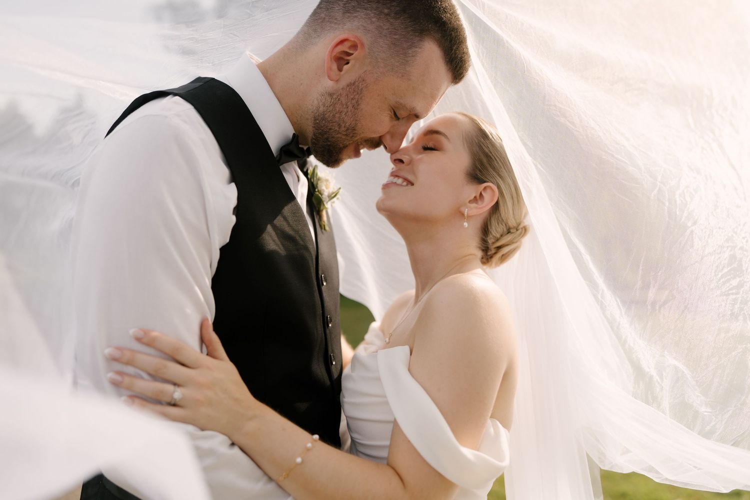 Bride and groom share an intimate forehead touch under a billowing white veil outdoors at Guelph golf club.