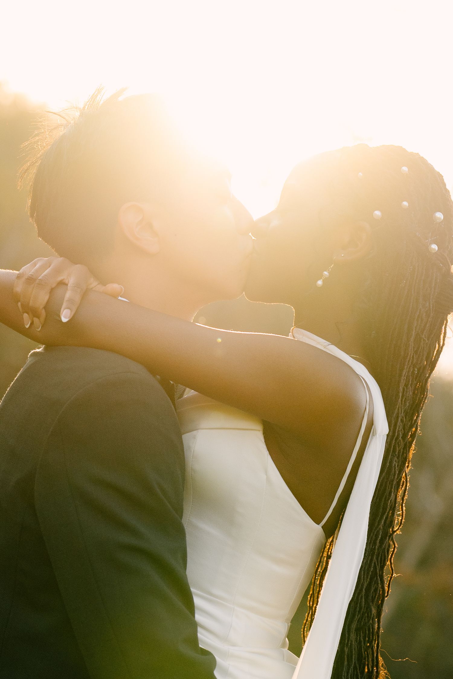 An interracial bride and groom share a romantic kiss bathed in warm golden sunset light outdoors at Wren House.