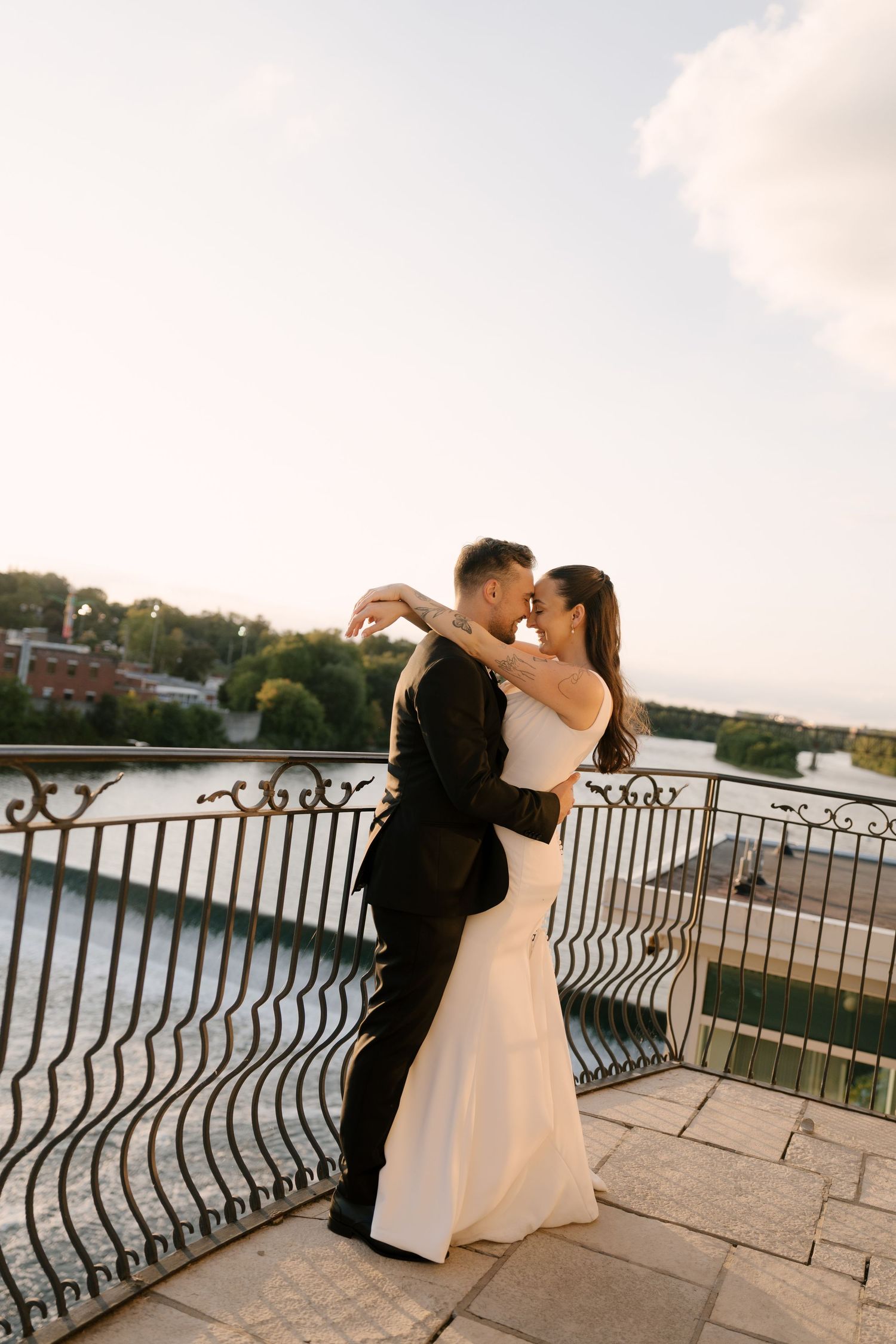 Bride and groom embracing romantically on a balcony overlooking a river at sunset at Cambridge Mill.