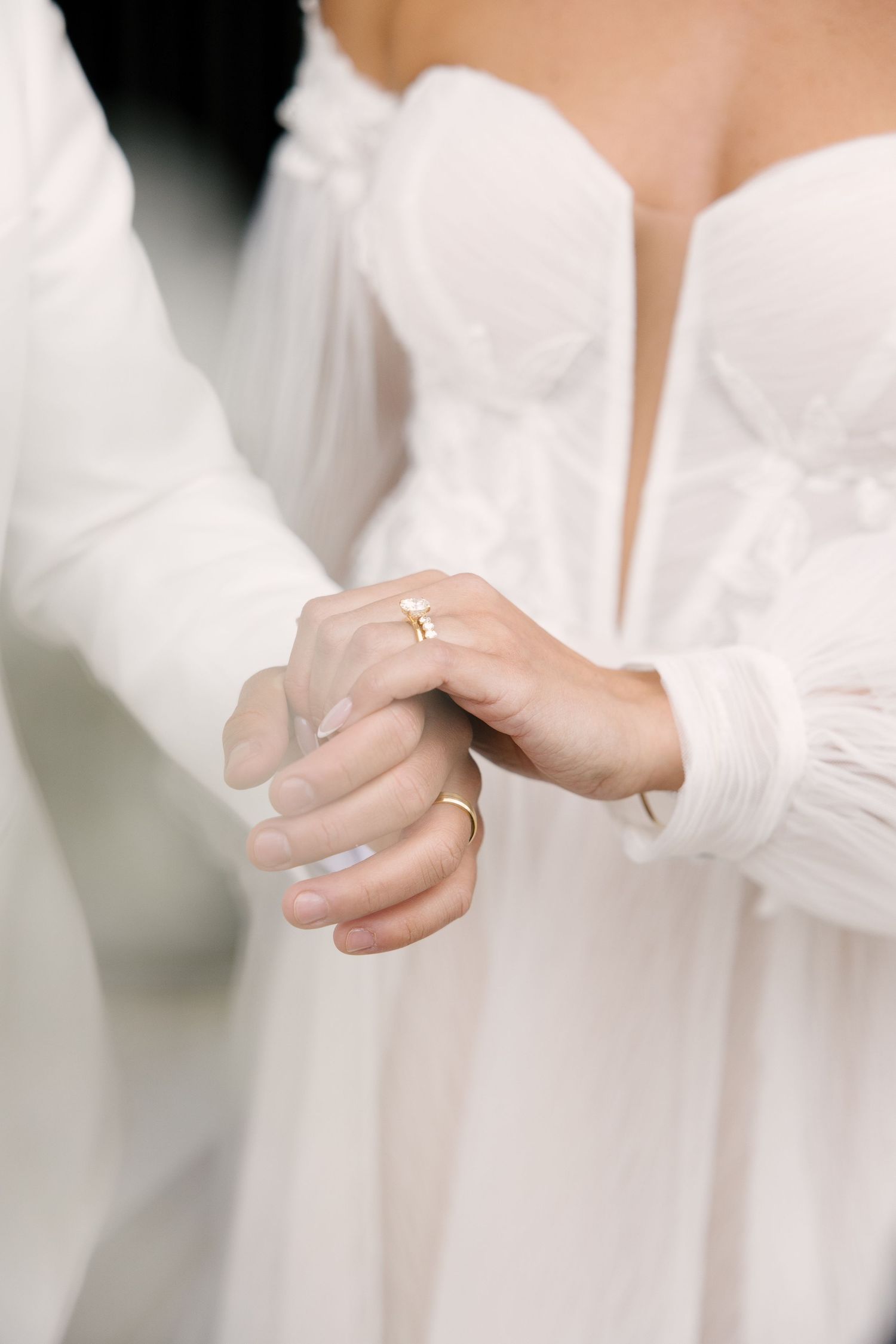 Close-up of bride and groom holding hands showing gold wedding rings and engagement ring.