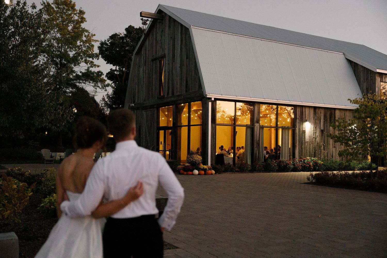 Bride and groom embracing outside a warmly lit barn wedding venue at dusk at Pillar and Post wedding venue.
