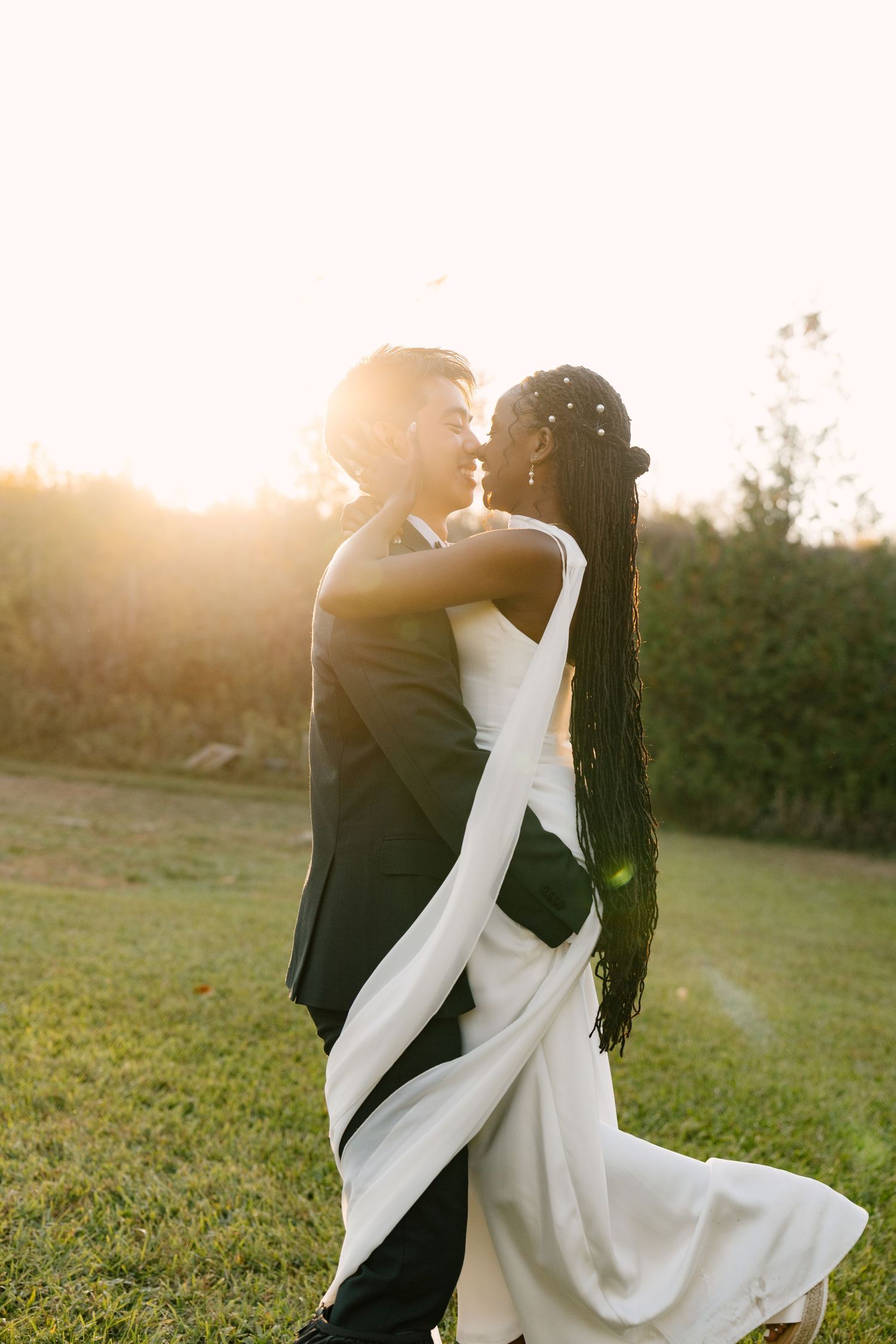 An interracial couple embraces and nearly kisses in a sun-drenched outdoor wedding portrait at golden hour at Wren House.