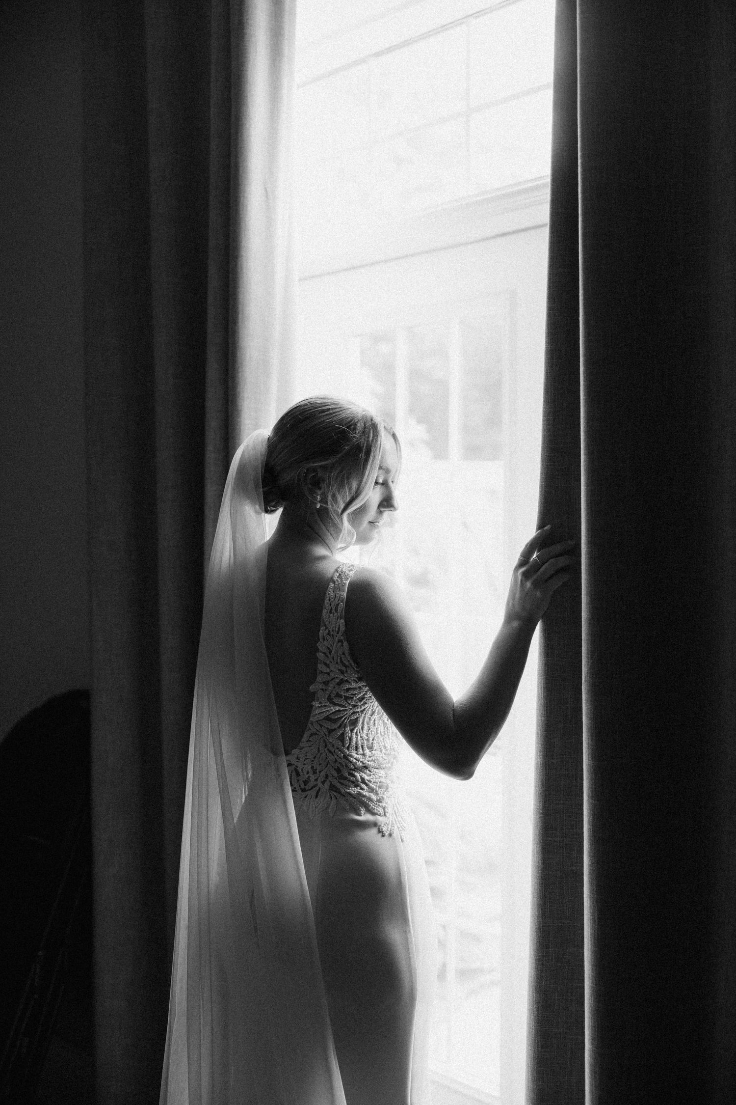 Elegant black and white silhouette of a bride in lingerie and veil standing by a window.