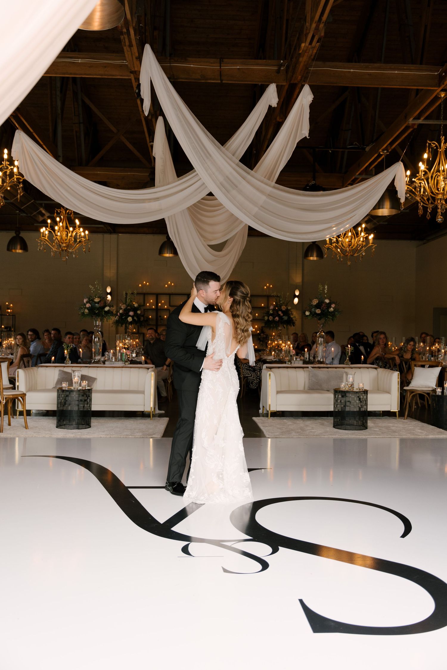 Bride and groom share first dance on white monogram dance floor in elegant ballroom with draped ceilings and chandeliers at St Marys.