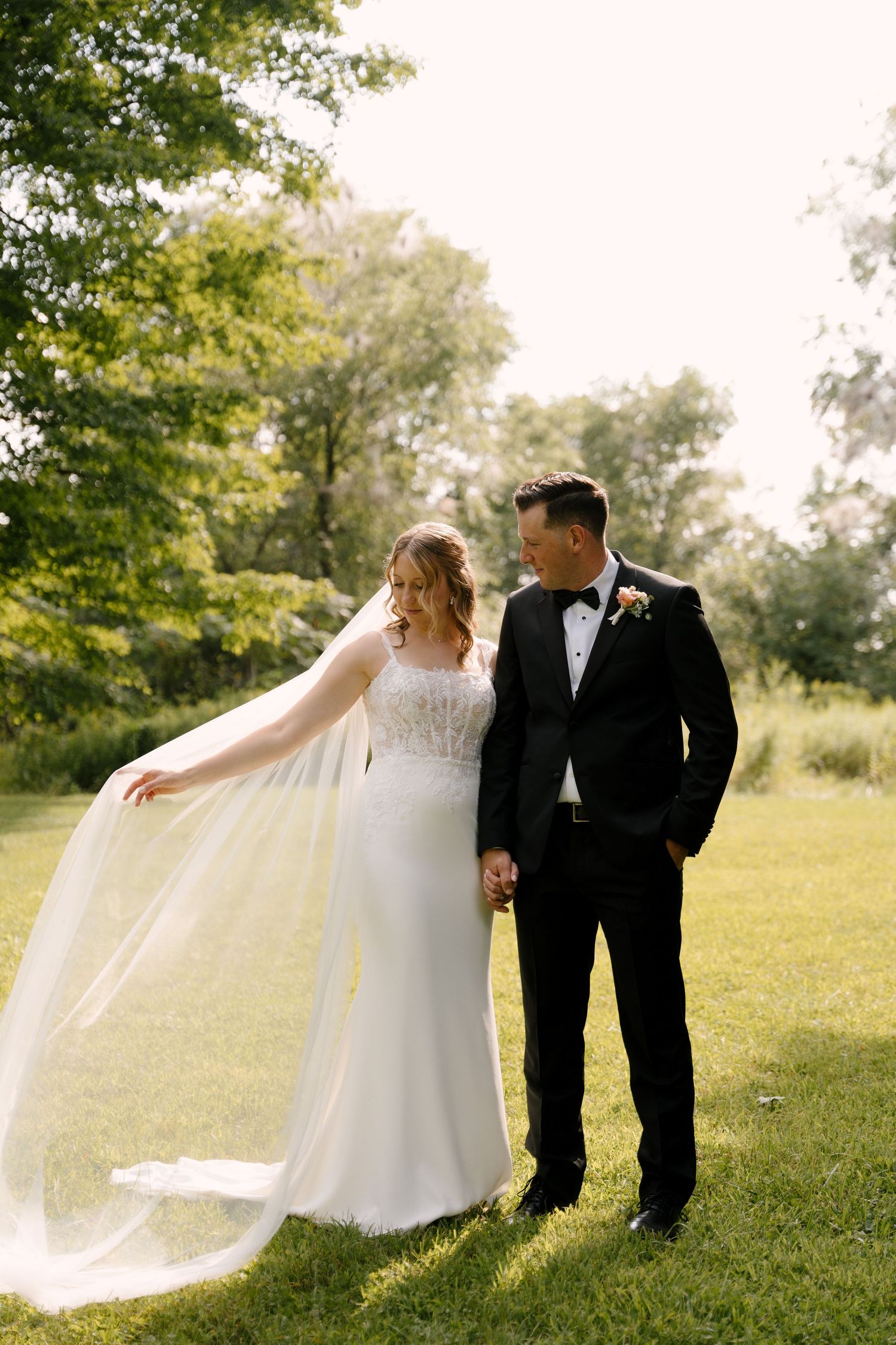 Bride twirls her veil while holding groom's hand in a sunlit garden on their wedding day.