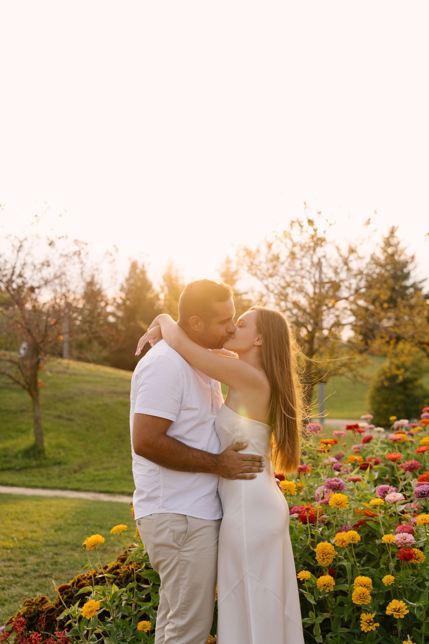 Couple kissing in a colorful flower garden at golden hour, surrounded by vibrant blooms and warm sunlight.