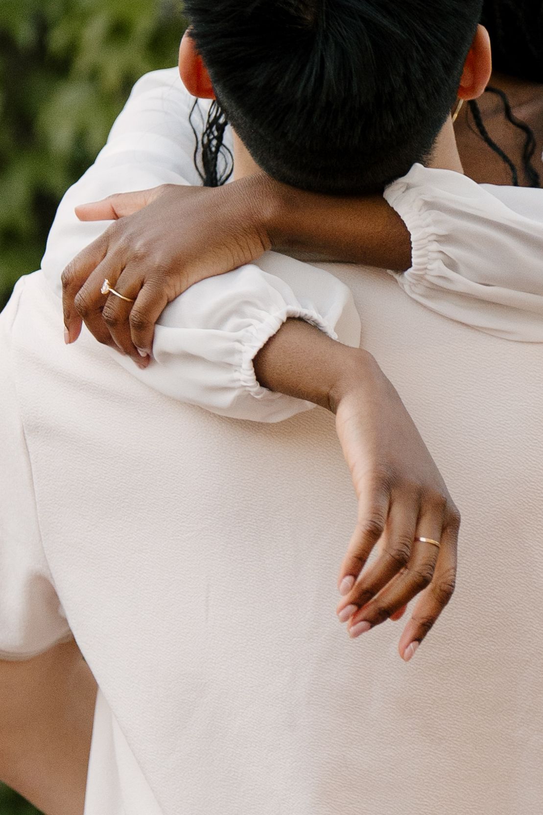 Close-up of woman's hands with rings wrapped around partner's back in an embrace.